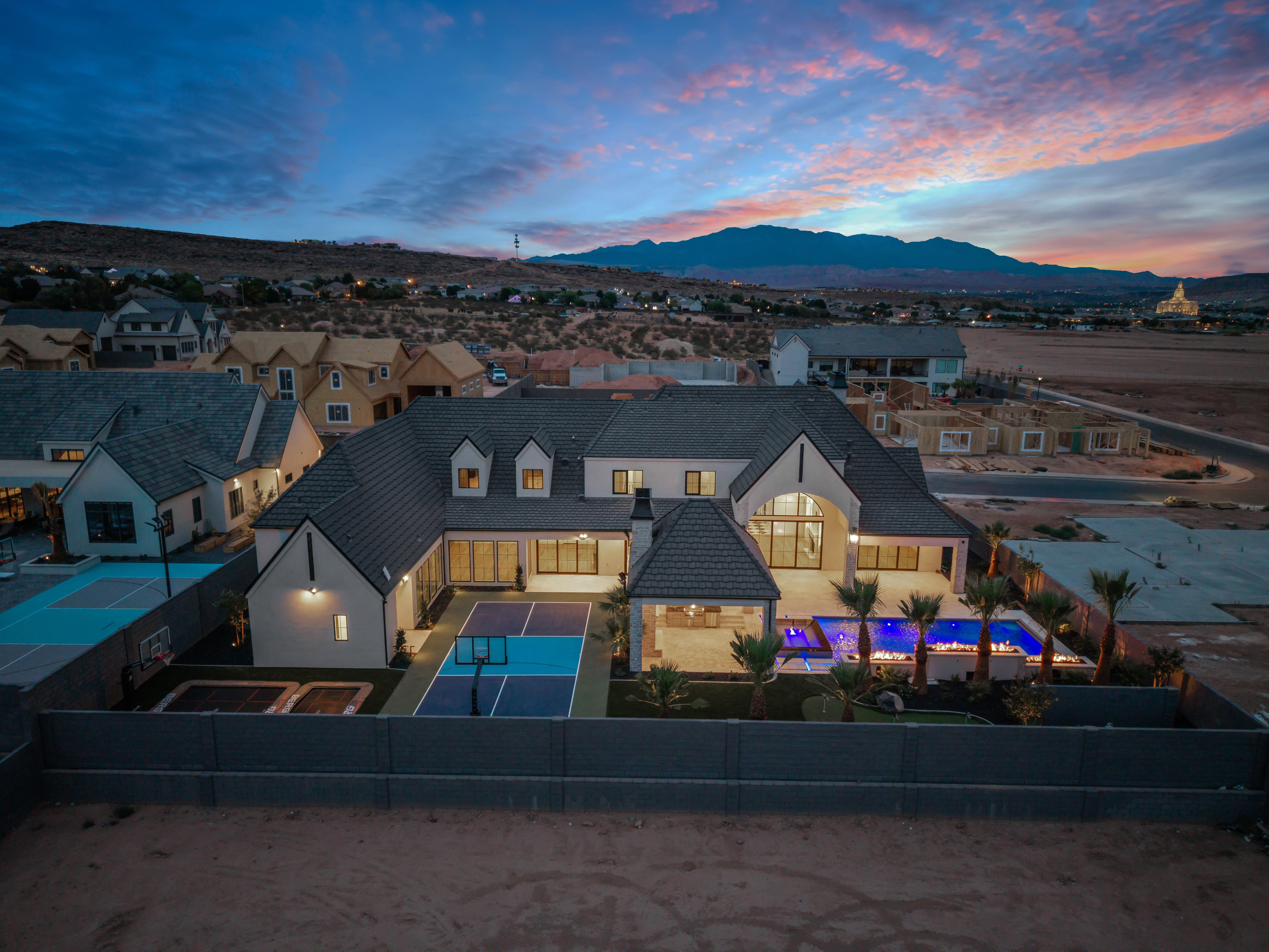 Contemporary residence featuring a dark tile roof, multiple dormer windows, a spacious backyard with a lighted pool, an outdoor covered patio, and a dedicated sport court