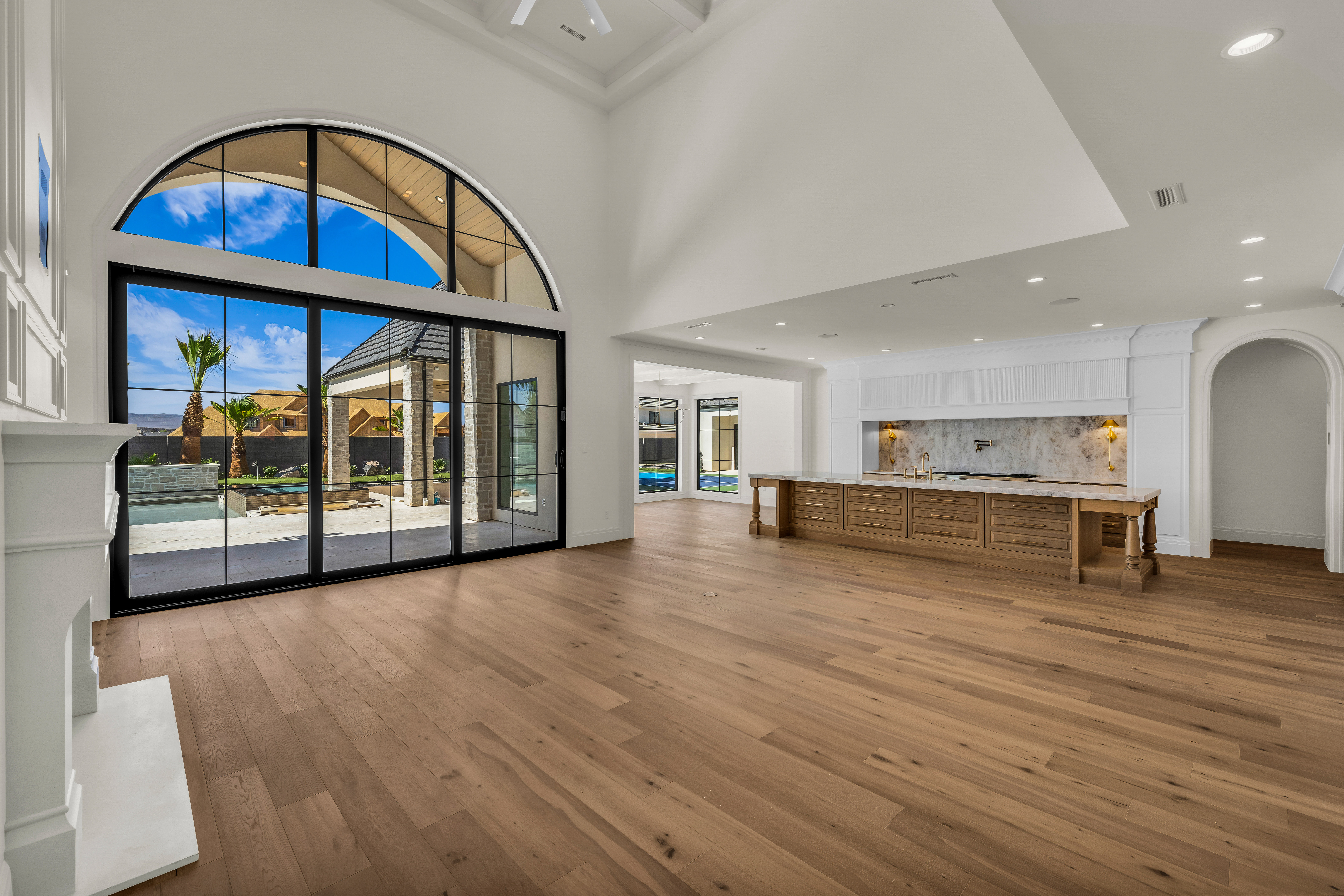 Expansive room featuring high vaulted ceilings, light wood-finish flooring, and a white fireplace mantel