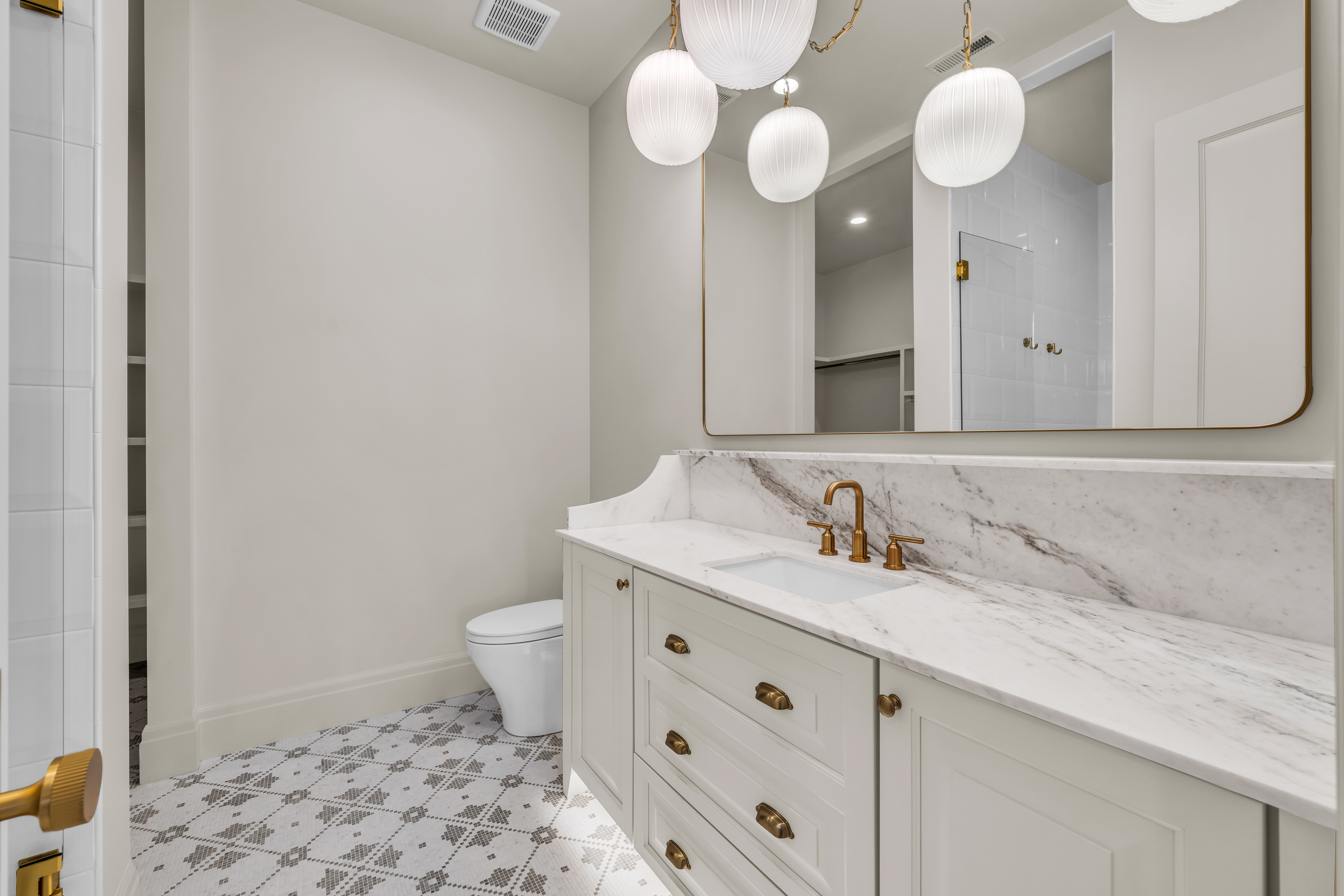 White vanity with an integrated sink, polished brass hardware, and a stone countertop extending to a full-height backsplash