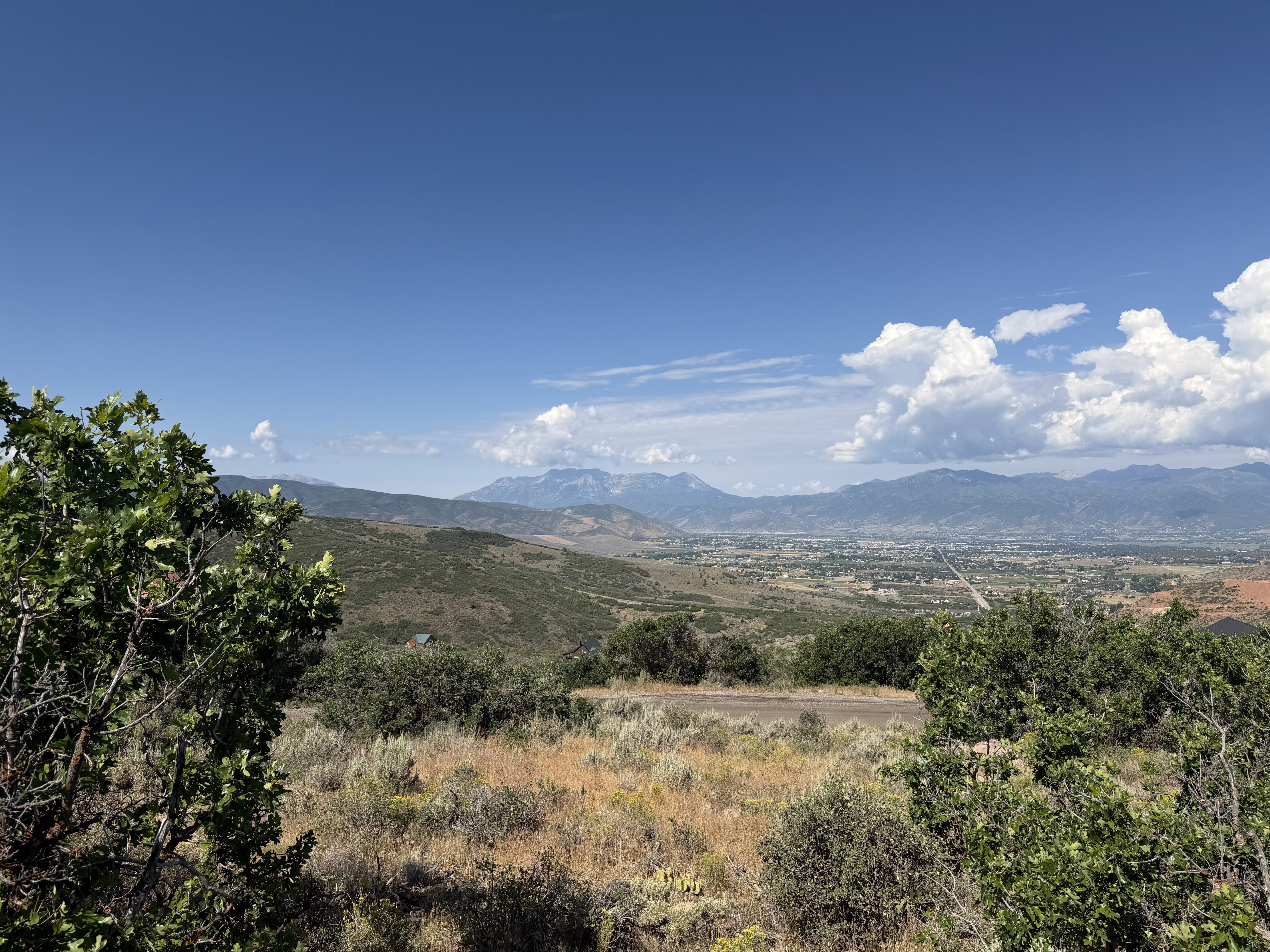 Expansive landscape featuring distant mountains, a broad valley, and a clear blue sky with scattered clouds