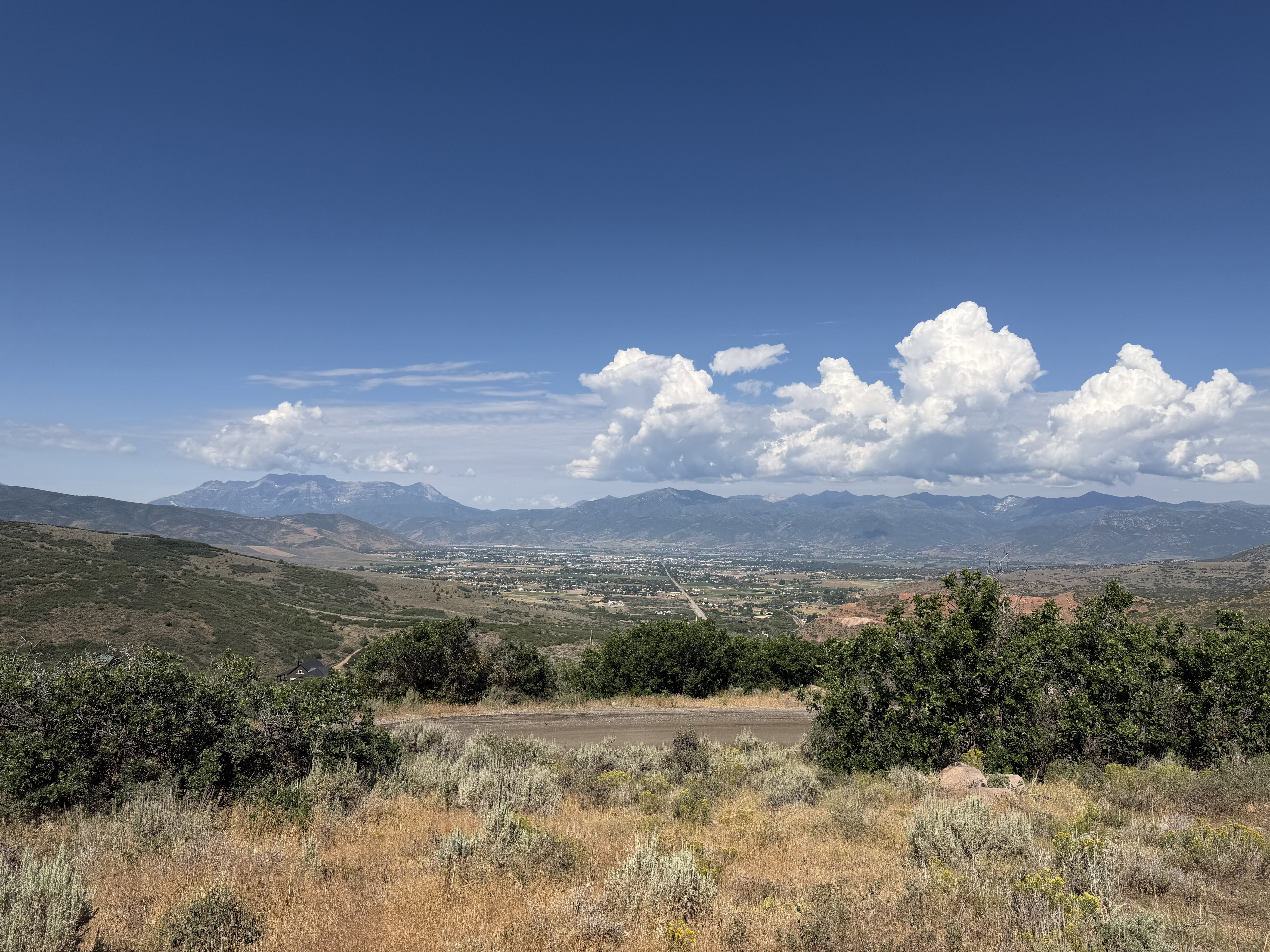 Expansive landscape featuring distant mountains, a valley settlement, and varied natural foliage
