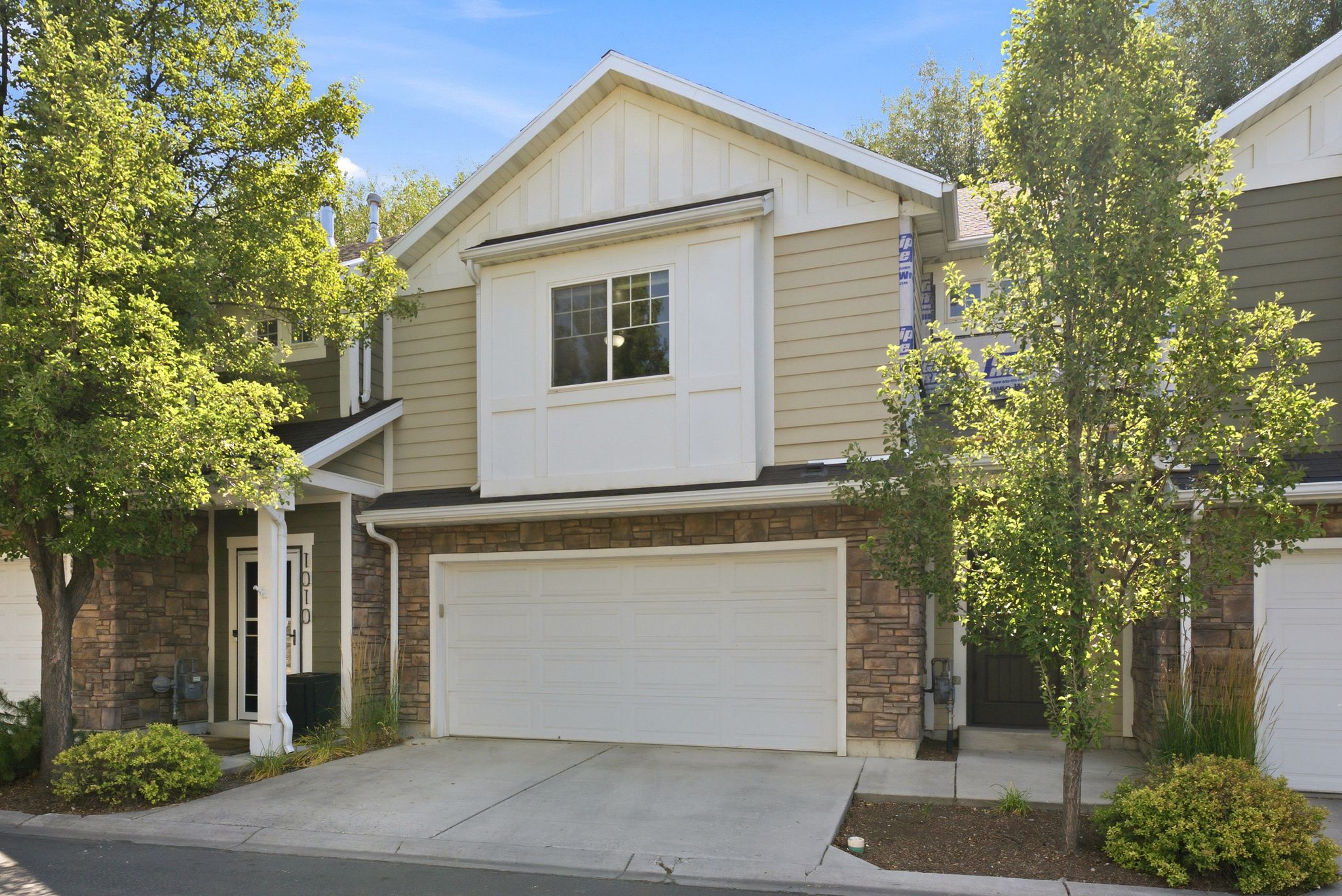 Multi-level townhome with a two-car garage, stone veneer, and horizontal siding