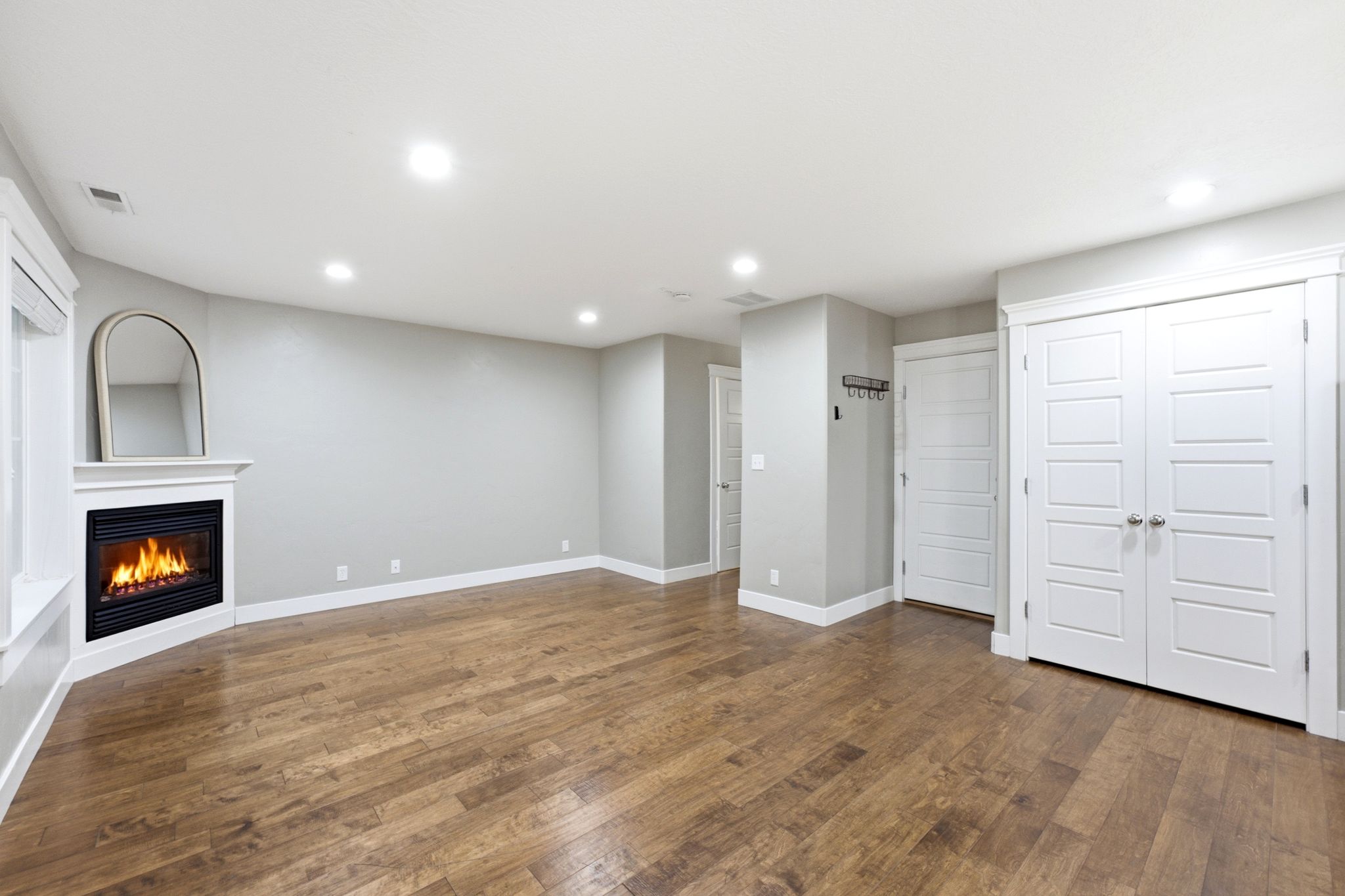 Spacious room featuring wood-finish flooring, a corner fireplace with white mantel, recessed lighting, and white bi-fold closet doors