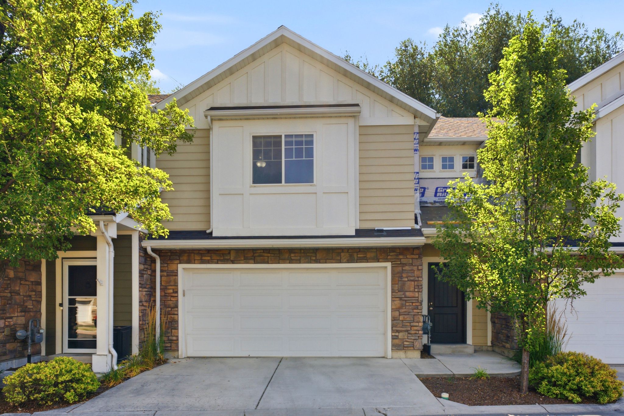 Multi-level townhouse exterior featuring a two-car garage, stone veneer accents, and light-colored siding