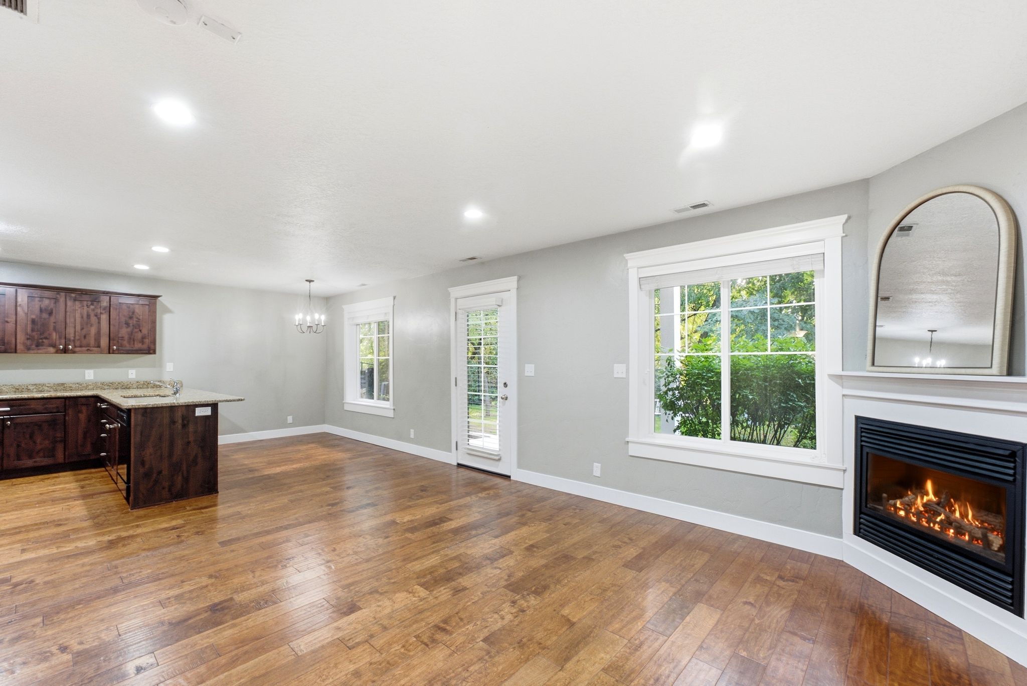 Open-concept living area featuring wood-finish flooring, a corner fireplace with a white mantel, and ample natural light from multiple windows