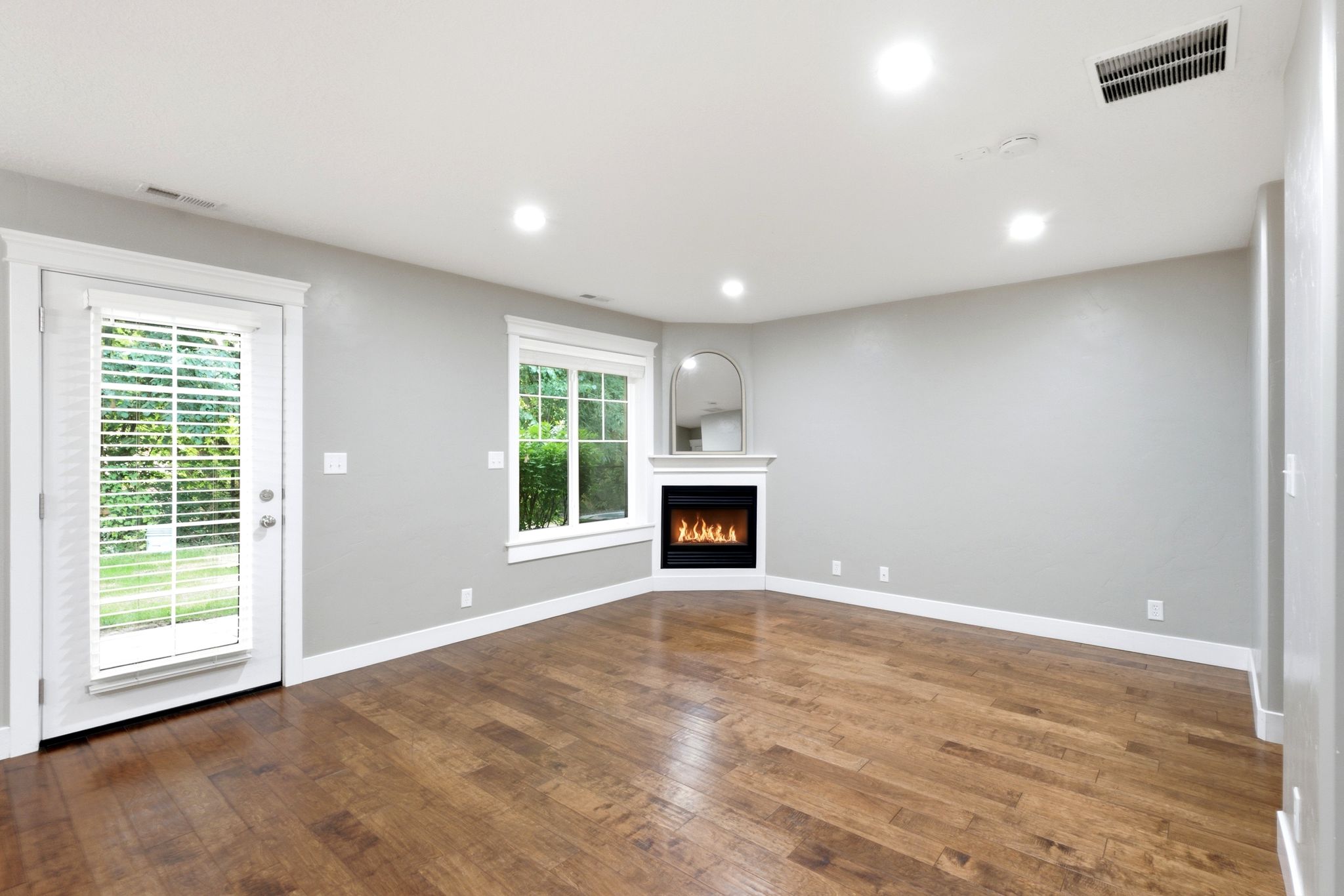 Spacious room featuring wood-finish flooring, a corner fireplace with a white mantel, and recessed lighting