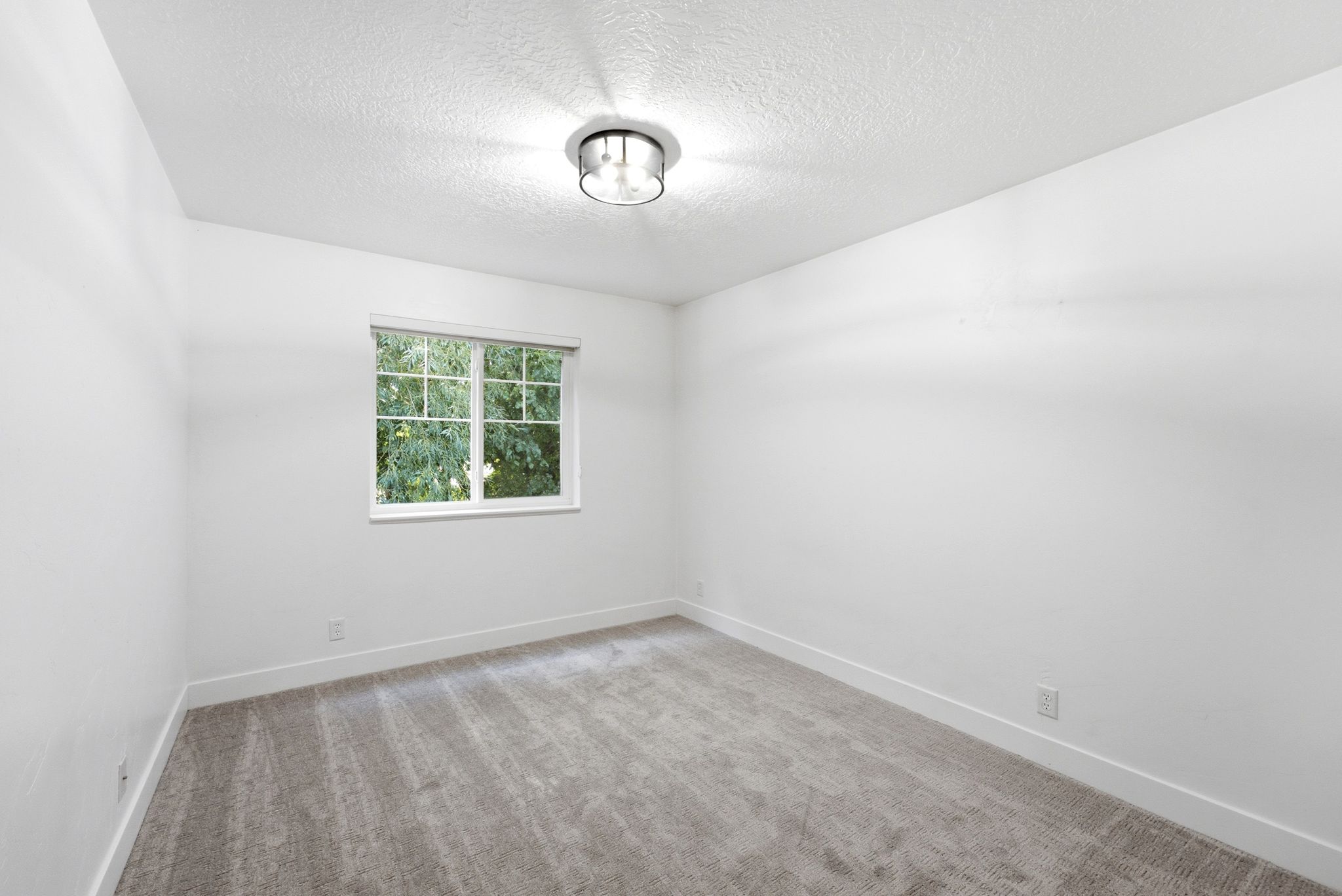 Bright room featuring light grey patterned carpeting, a white window frame, and a flush-mount ceiling light fixture with a brushed metal finish