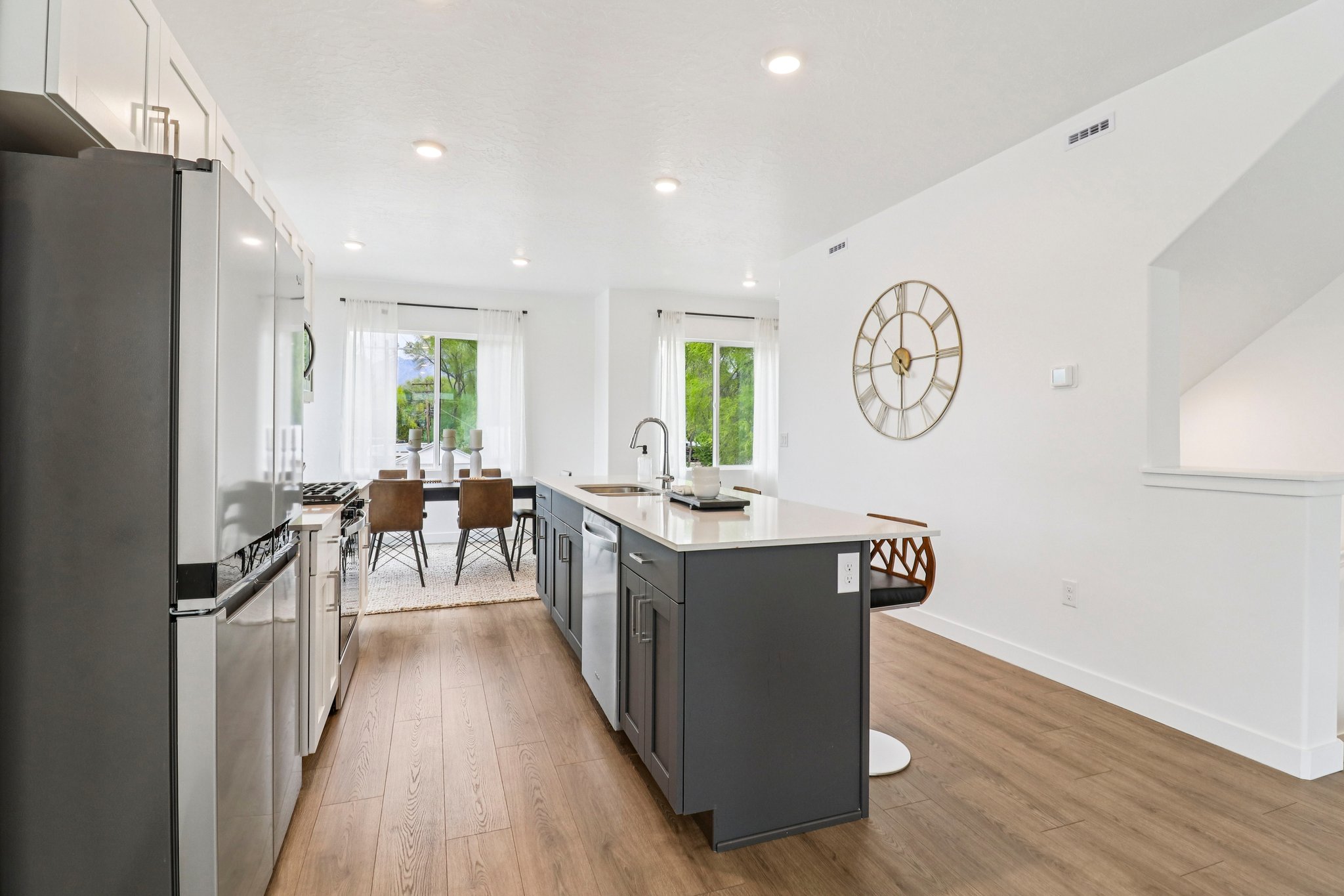 Modern kitchen featuring a central island with a sink, stainless steel appliances, white upper cabinetry, and contrasting gray lower cabinetry