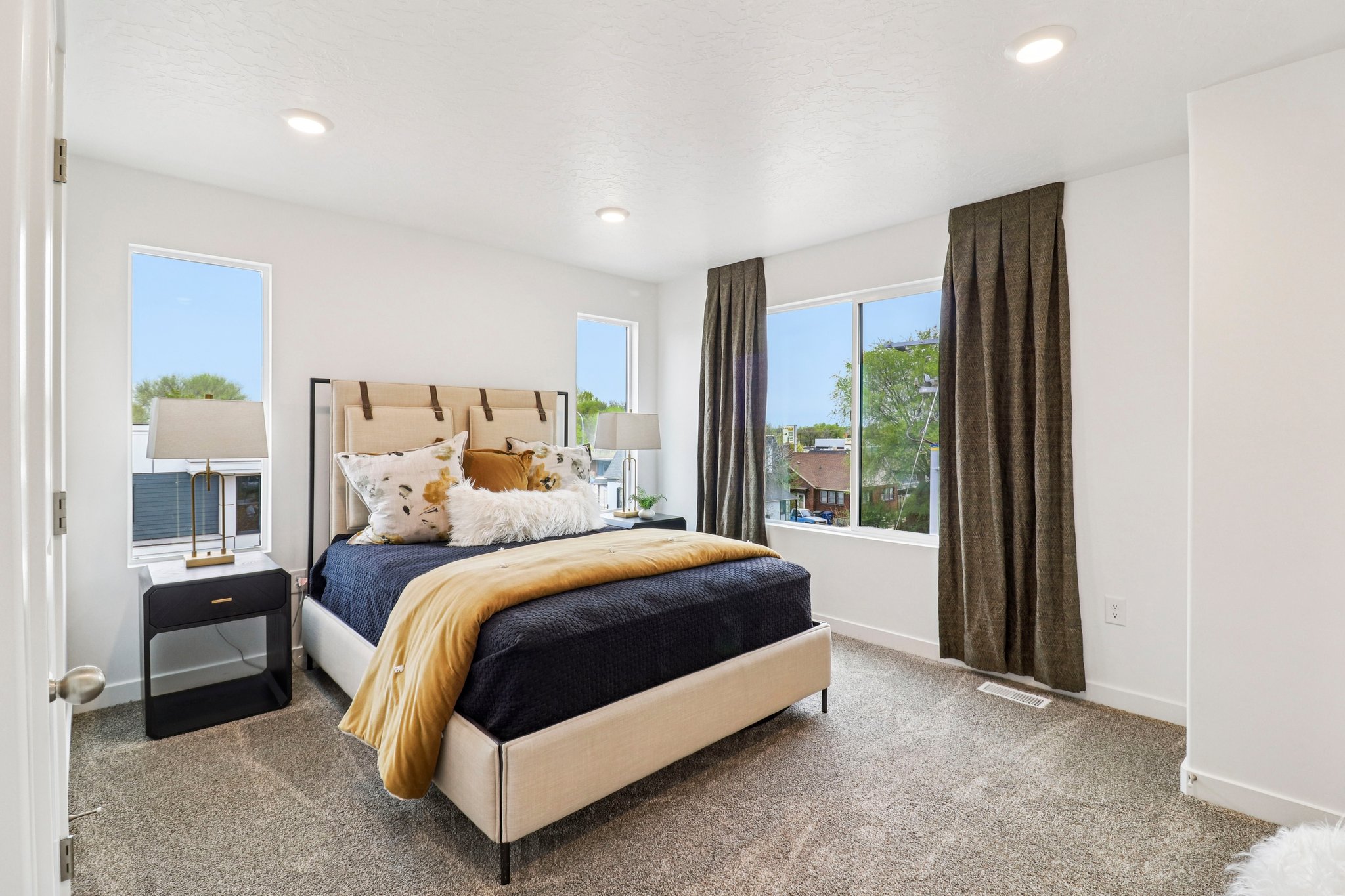Bright bedroom featuring recessed lighting, plush carpet flooring, white walls, and multiple large windows with neutral drapes