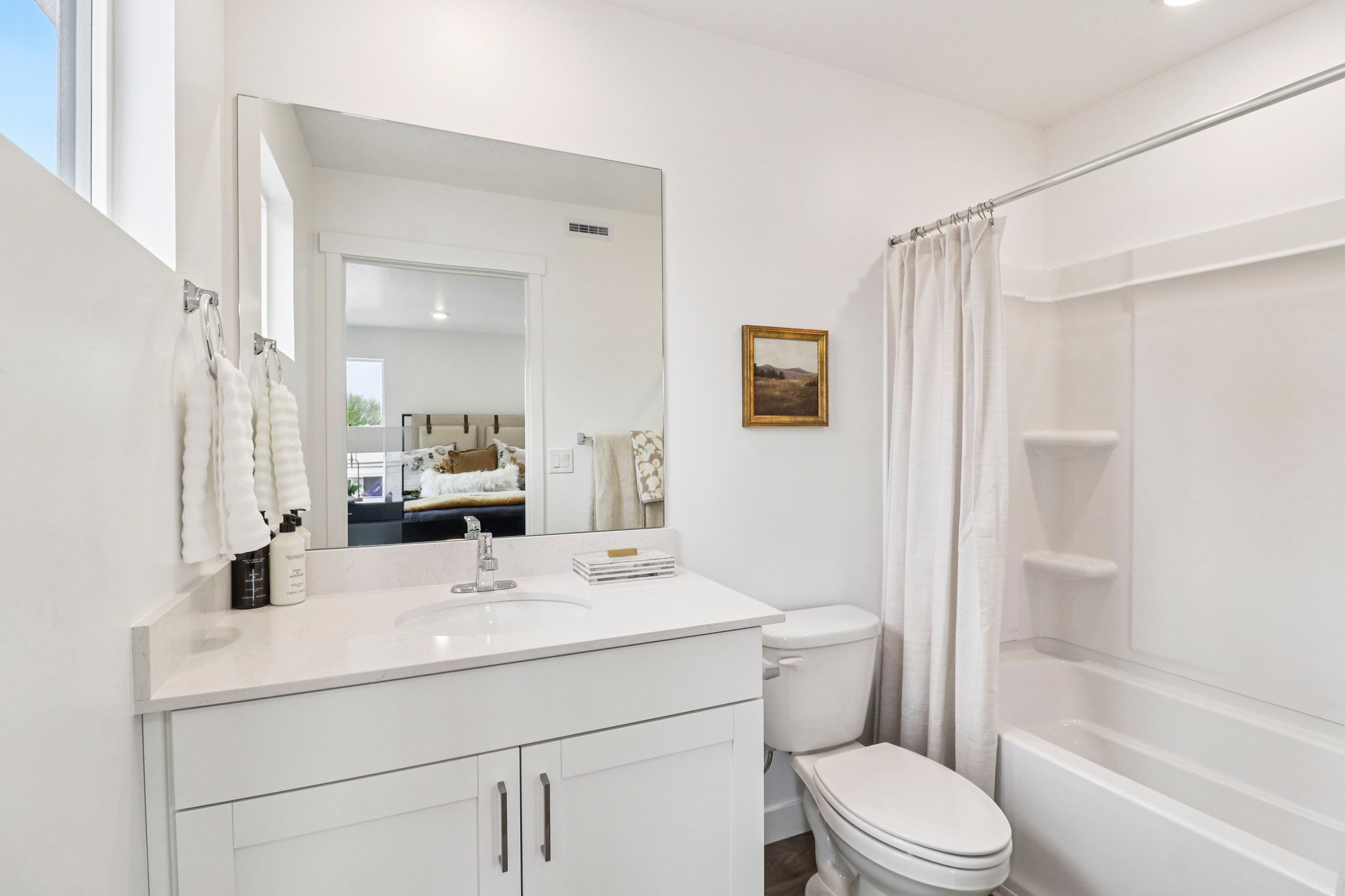 Bright bathroom featuring a single vanity with a white countertop and undermount sink, a large wall-mounted mirror, and a white toilet