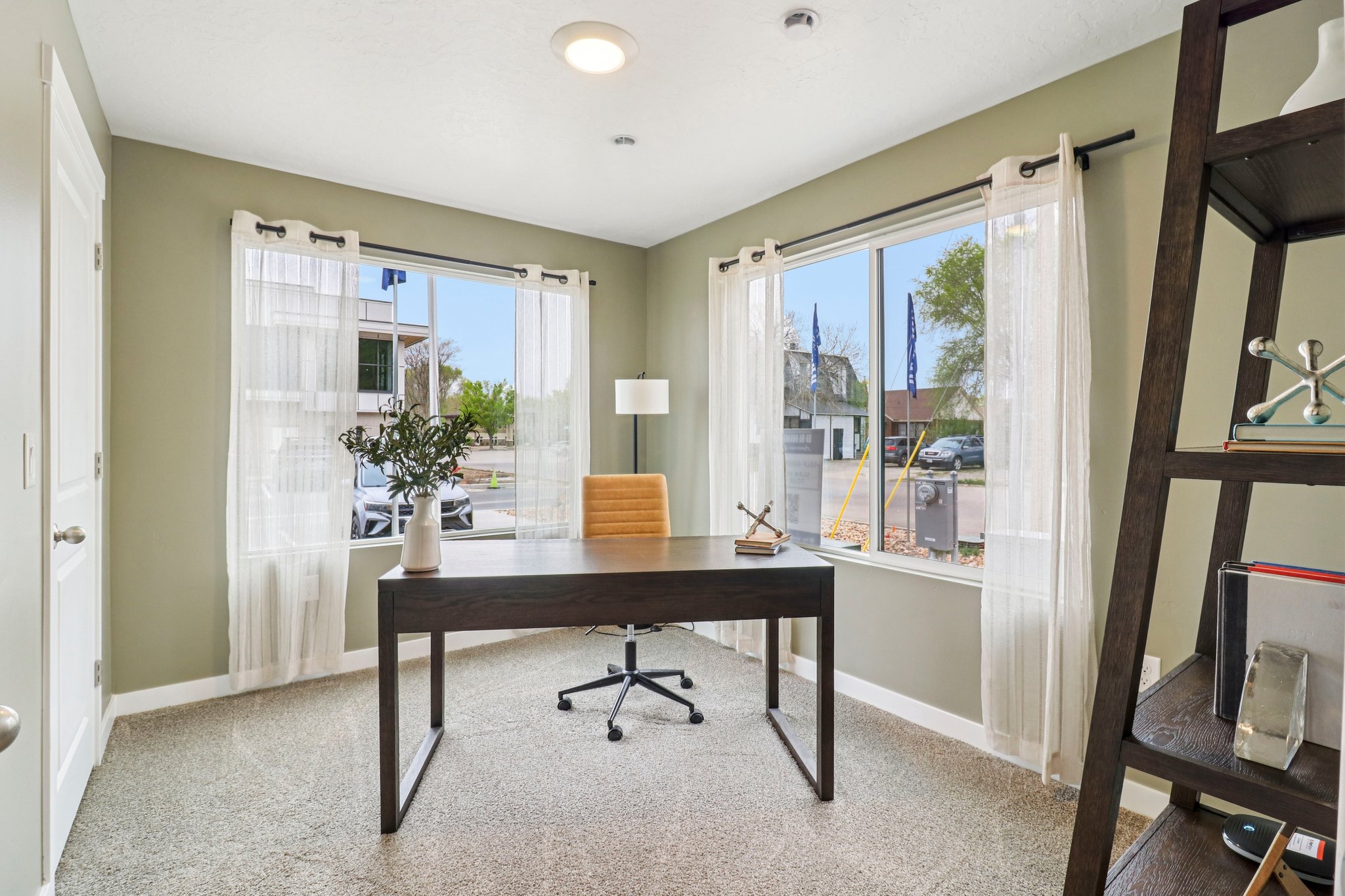 Room with light green walls, two large windows, recessed ceiling lighting, and light-colored carpet flooring