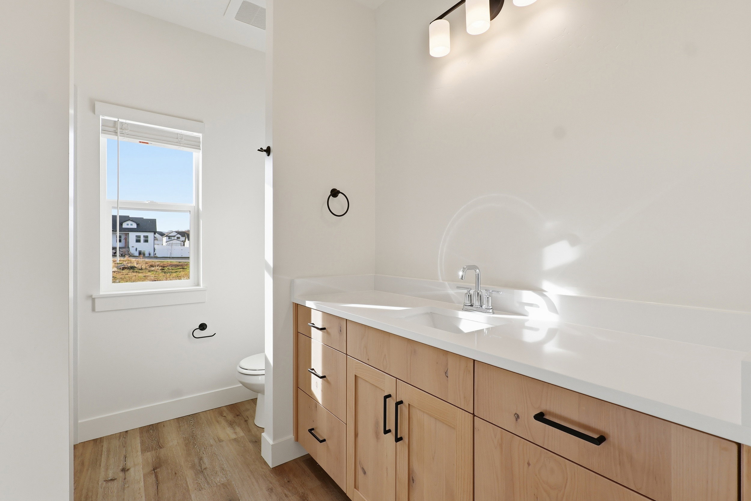 Bathroom vanity featuring light wood-finish cabinetry, a white countertop with an integrated sink, and matte black hardware
