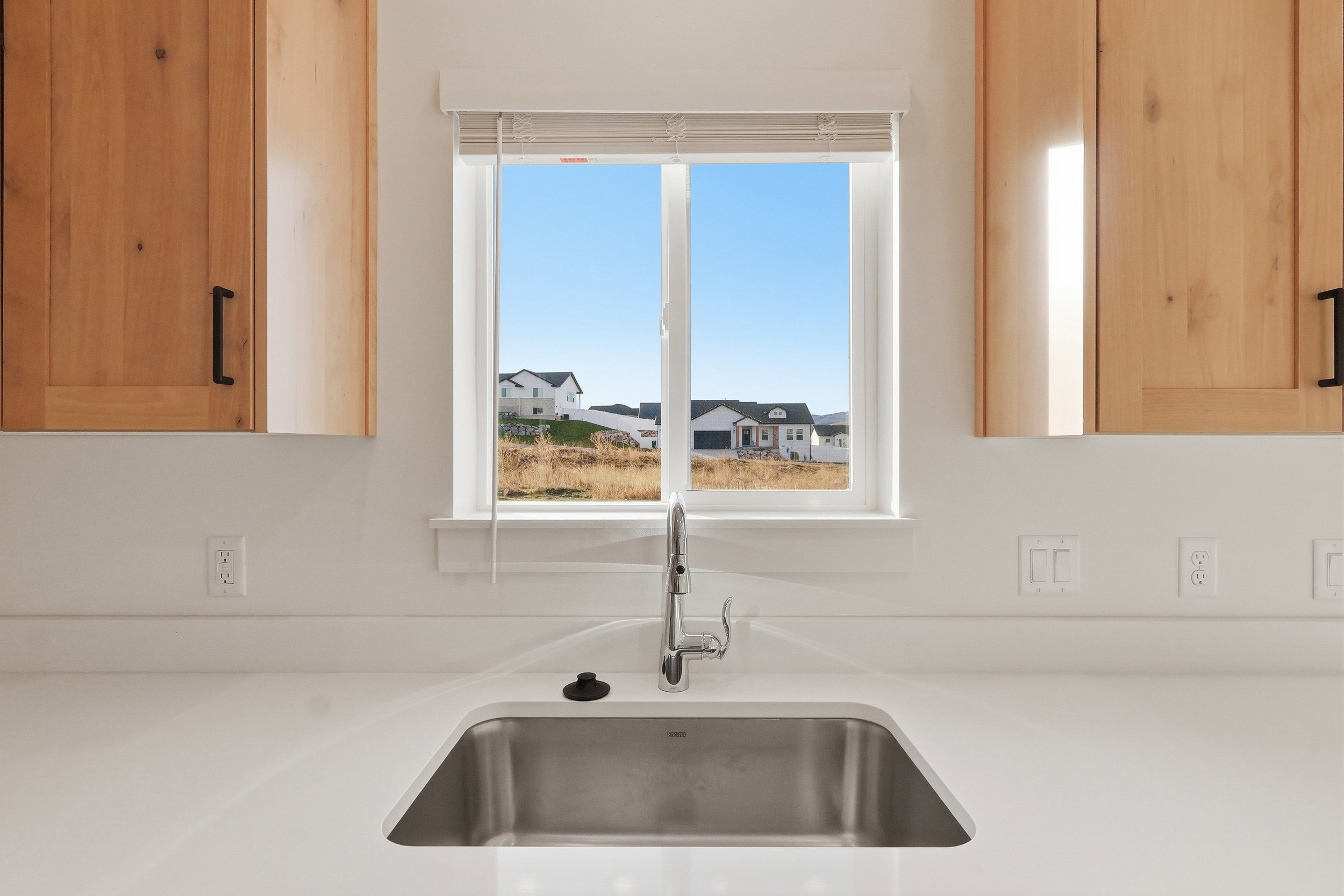 Kitchen sink area featuring a stainless steel undermount sink, a single-handle faucet, and a white solid surface countertop