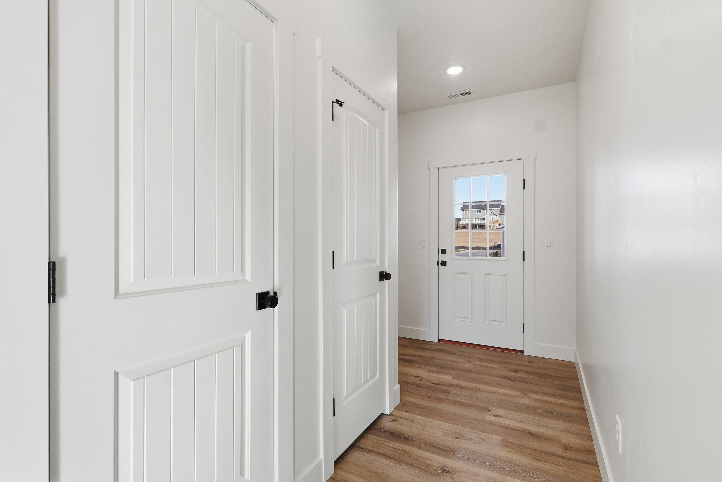 Entryway featuring wood-finish flooring, white paneled doors with matte black hardware, a multi-pane glass door, and recessed lighting
