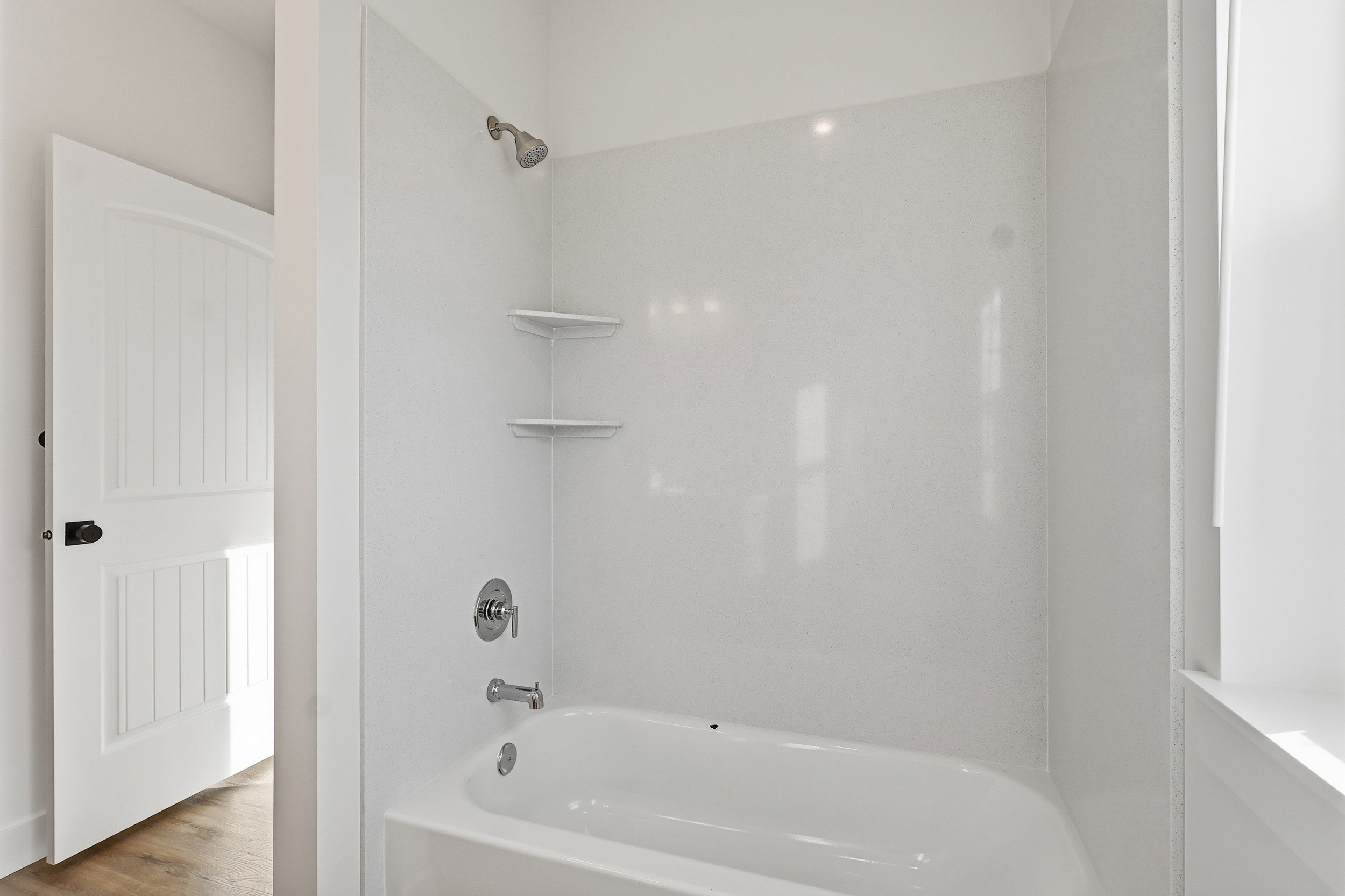 Bathtub-shower combination featuring a white surround, chrome fixtures, and built-in corner shelving