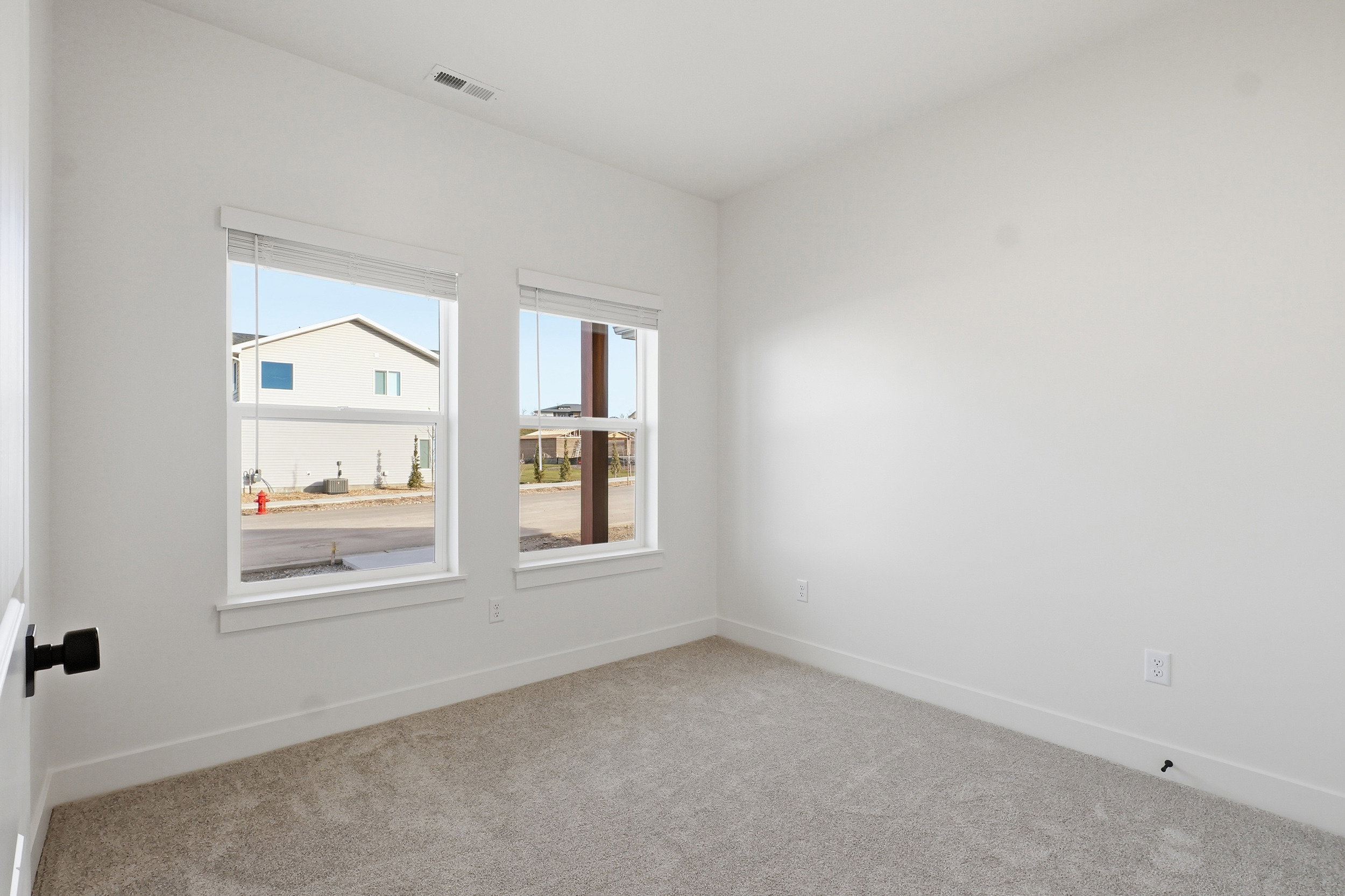 Neutral-toned carpeted room featuring white walls and two double-hung windows with blinds