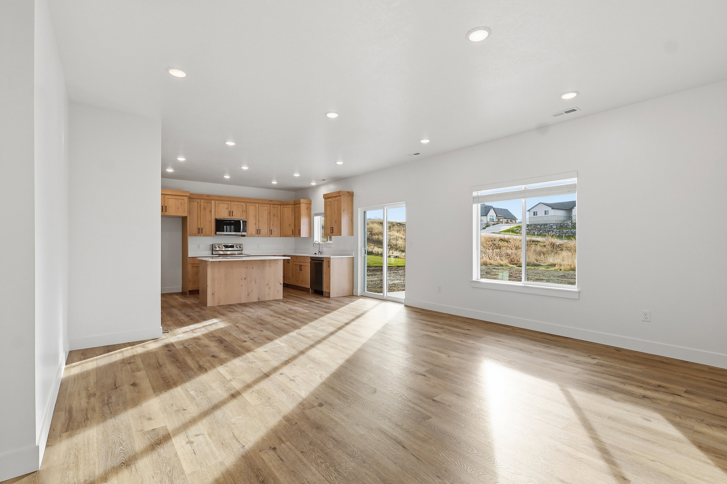 Open-concept living area with wood-finish flooring, recessed lighting, and a kitchen featuring light wood cabinetry and a central island