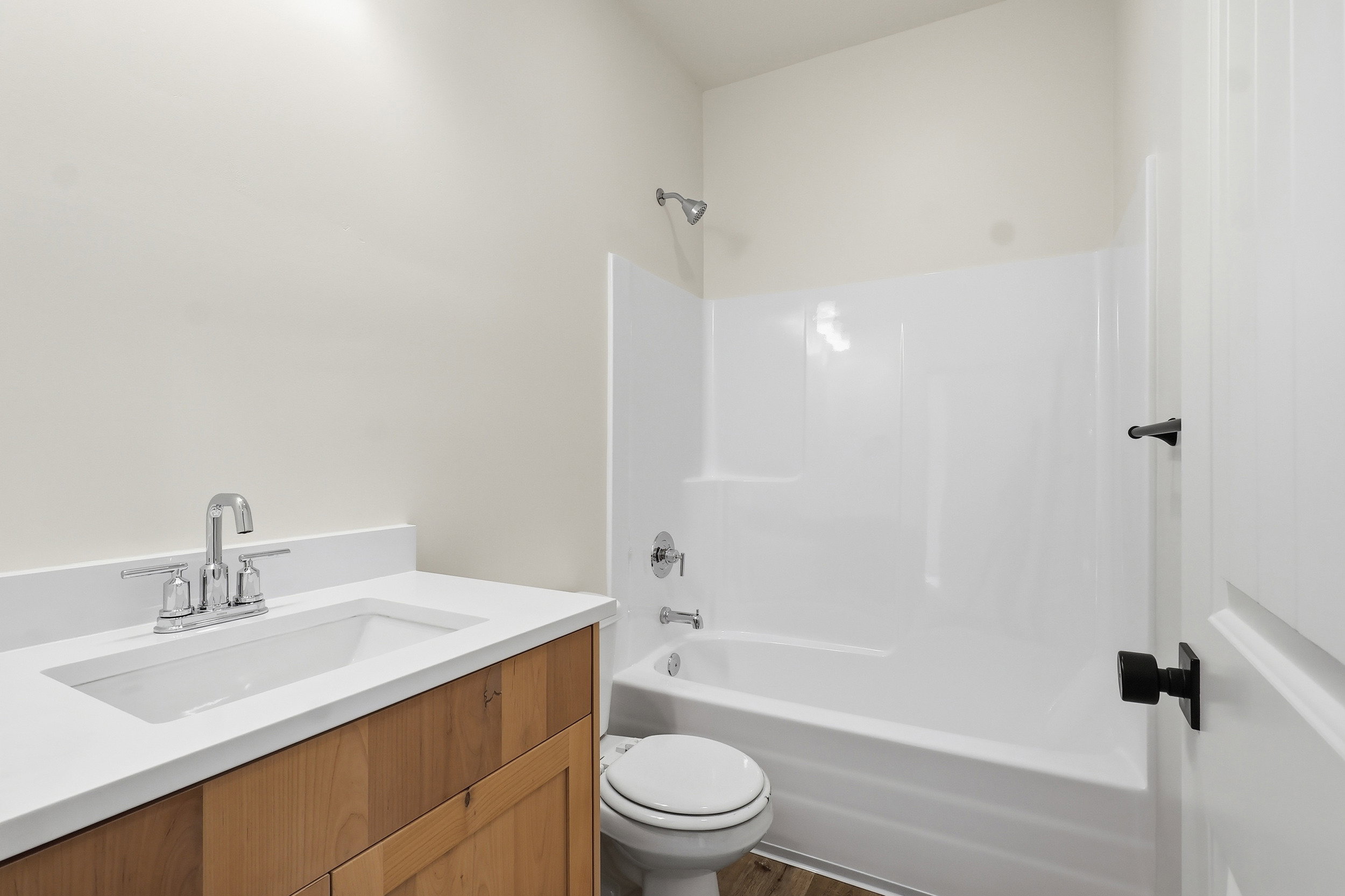 Bathroom featuring a wood-panel vanity, white countertop with integrated sink, chrome faucet, and a white tub/shower combination