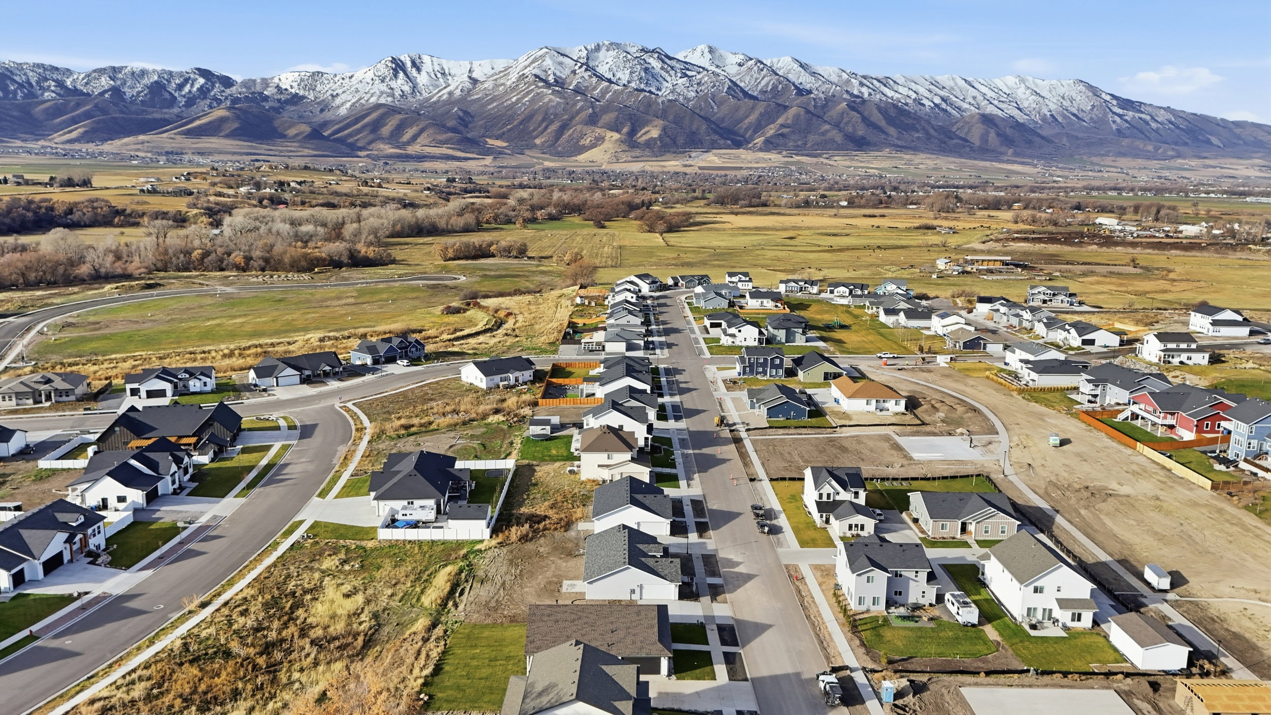 Newly developed residential area with paved streets and sidewalks, featuring a variety of single-family homes with diverse architectural styles, against a backdrop of snow-capped mountains
