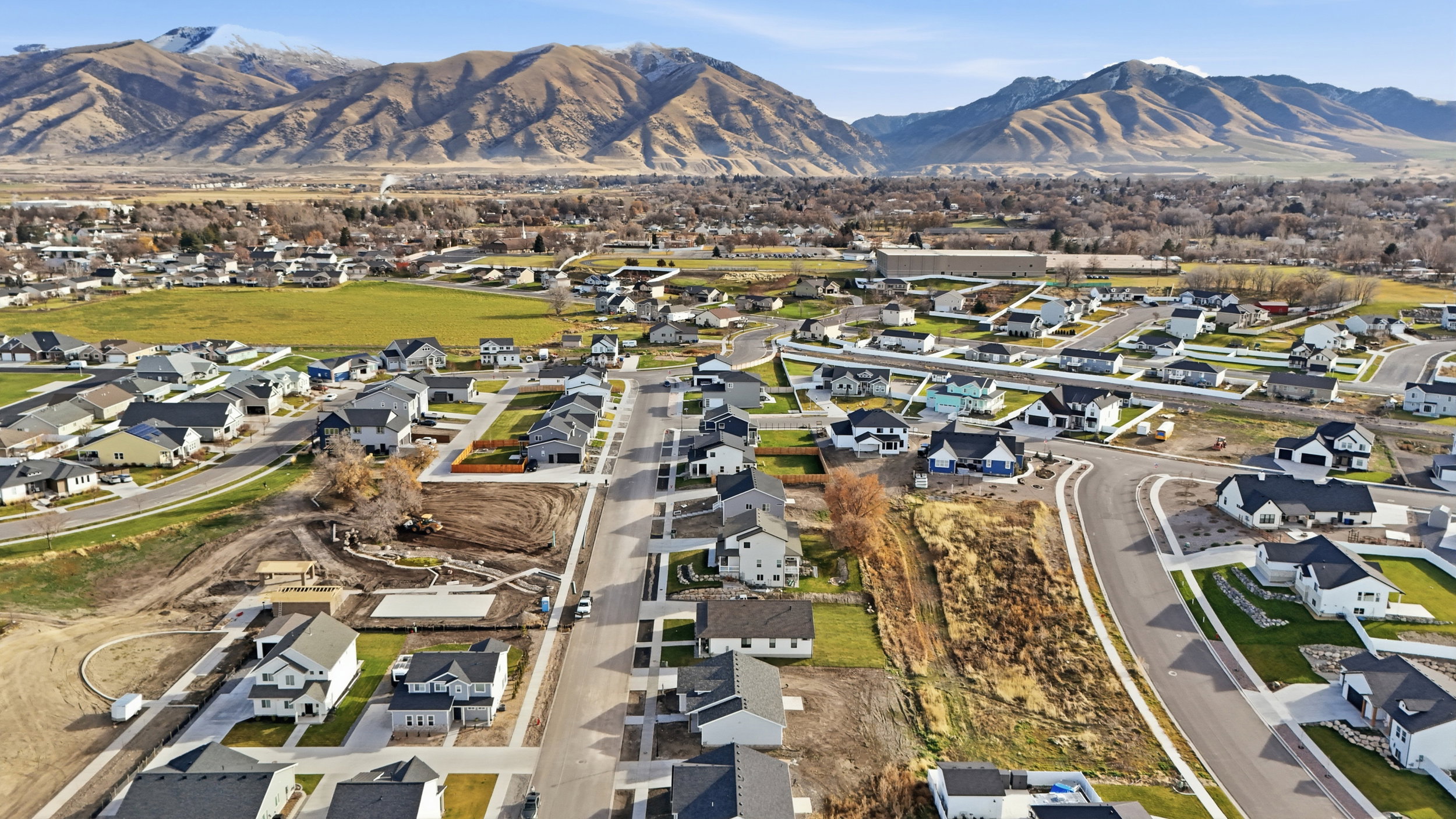 Expansive residential development featuring newly constructed homes with modern architecture, paved streets, and manicured lawns, all set against a backdrop of distant mountains