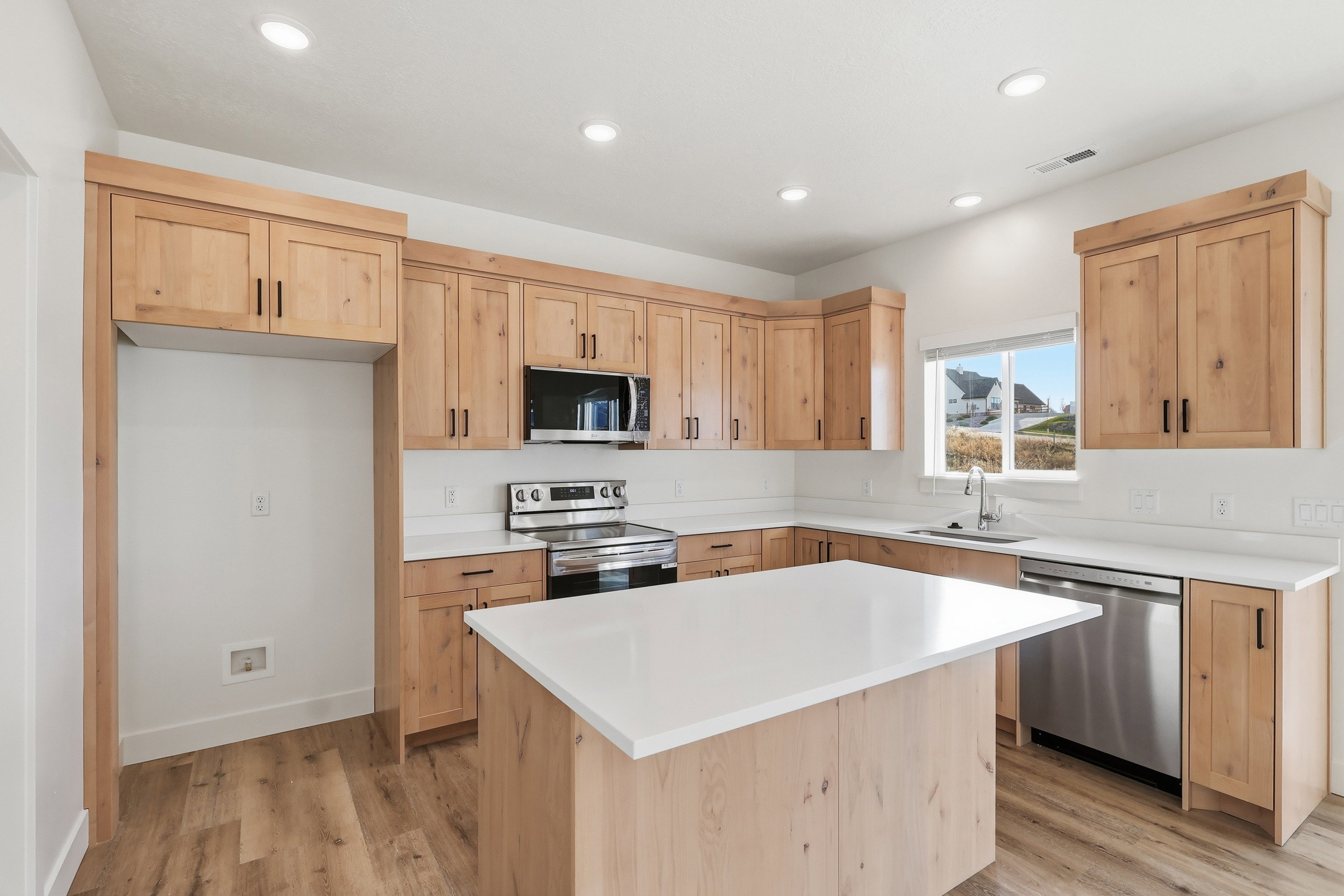 Modern kitchen featuring a central island with a white countertop, wood-finish flooring, recessed lighting, and stainless steel appliances