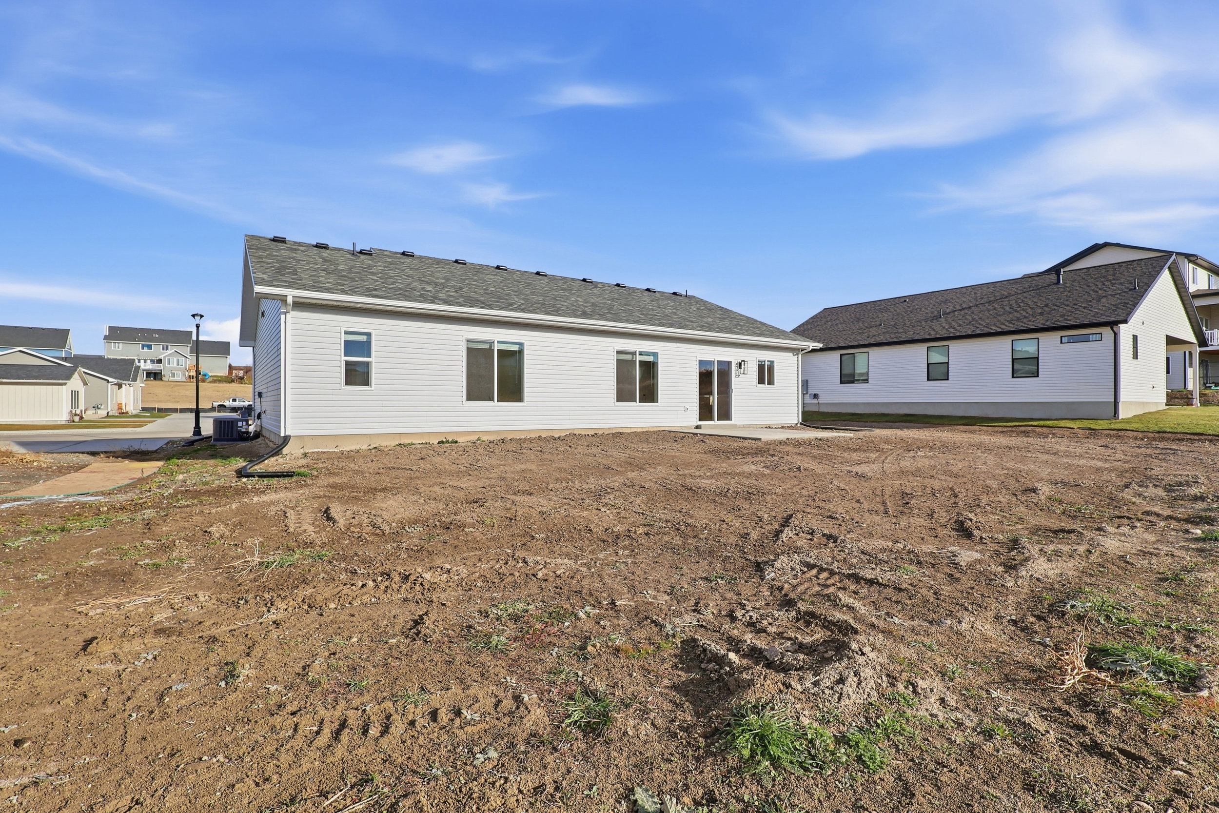 Spacious graded lot featuring a newly constructed residence with white siding, dark-framed windows, and a patio with sliding glass doors