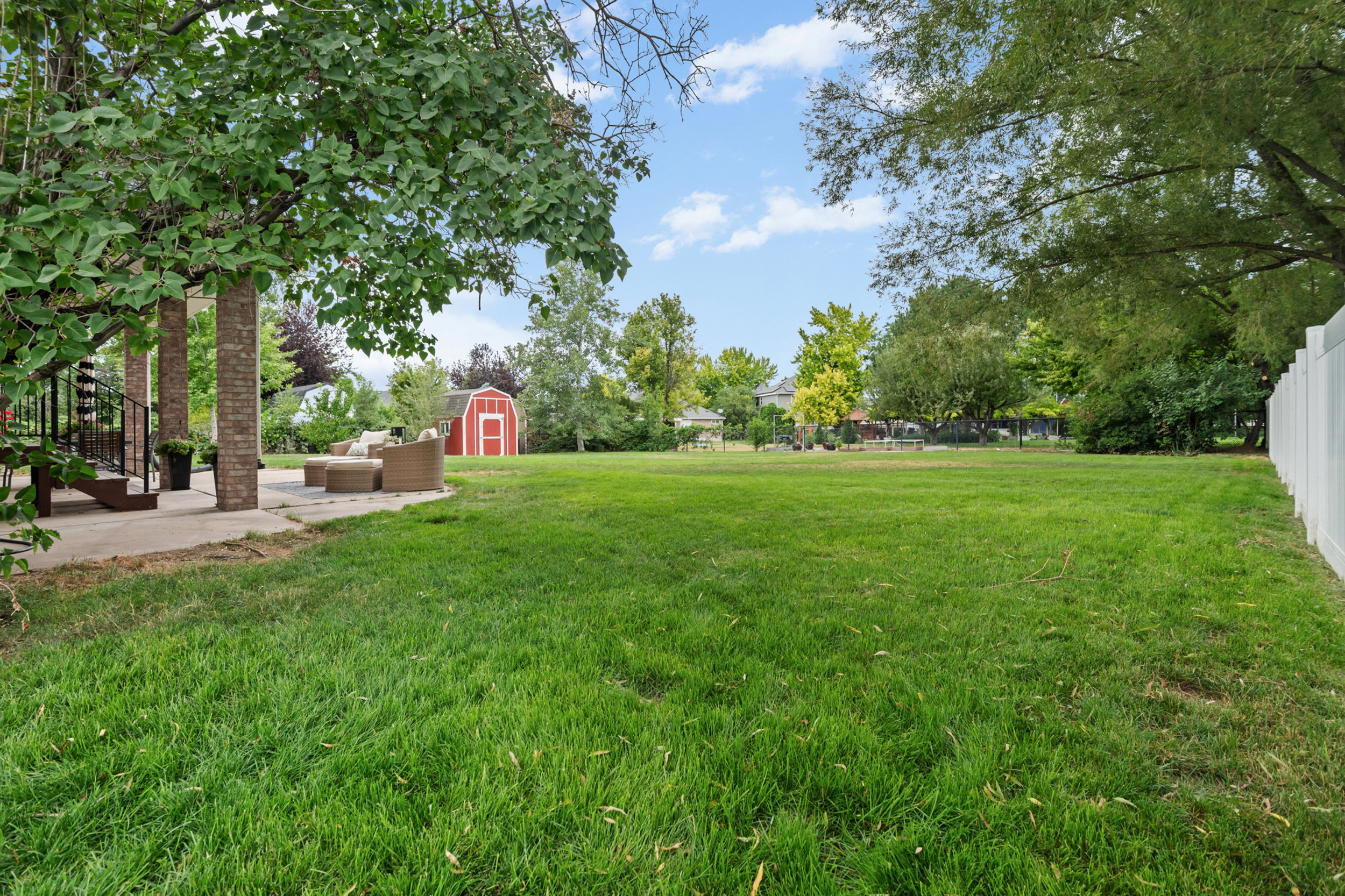 Expansive green lawn with mature trees and a detached red shed