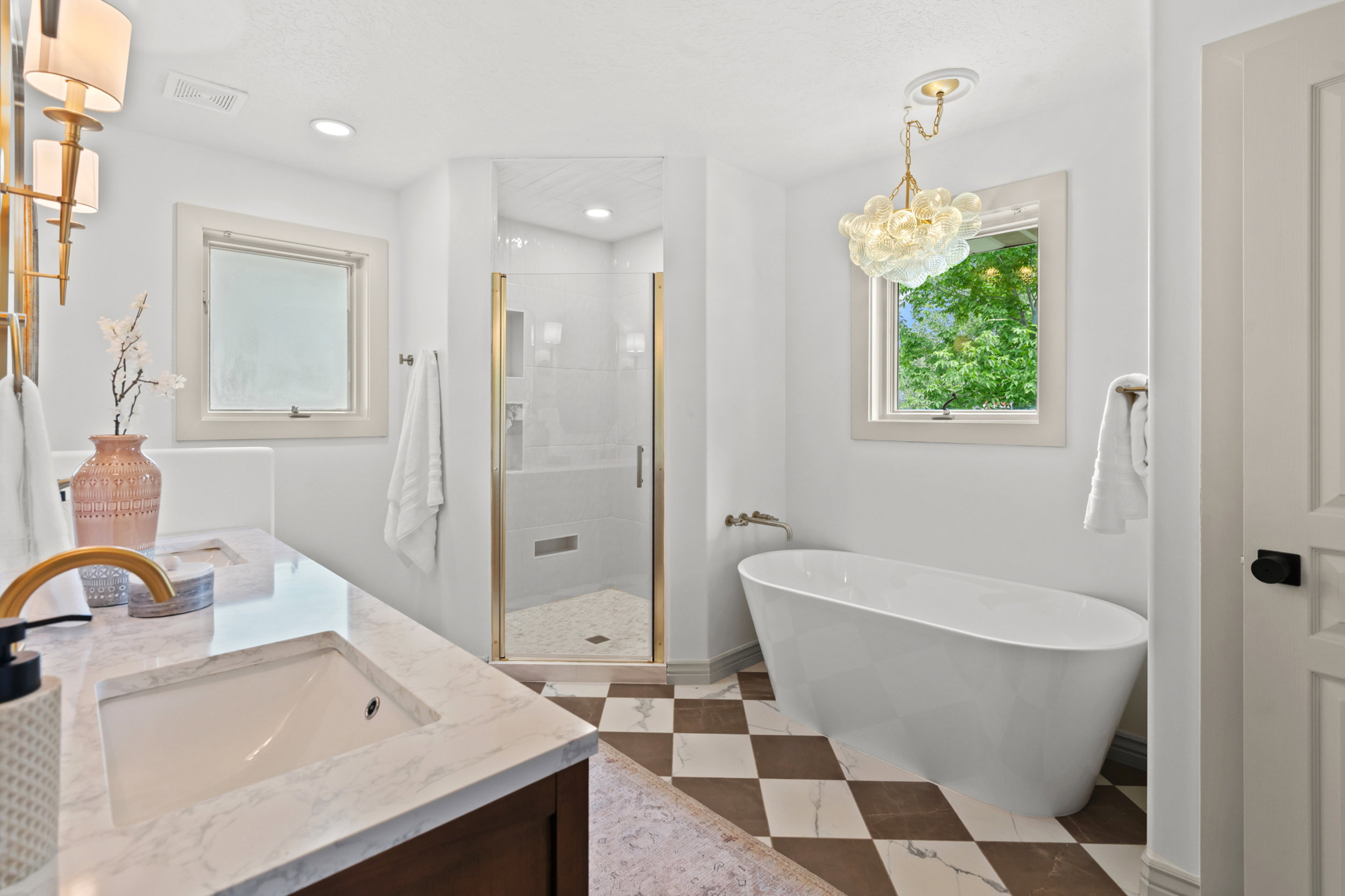 Spacious bathroom featuring a freestanding soaking tub, a glass-enclosed shower with gold-toned hardware, and a double vanity with a stone countertop