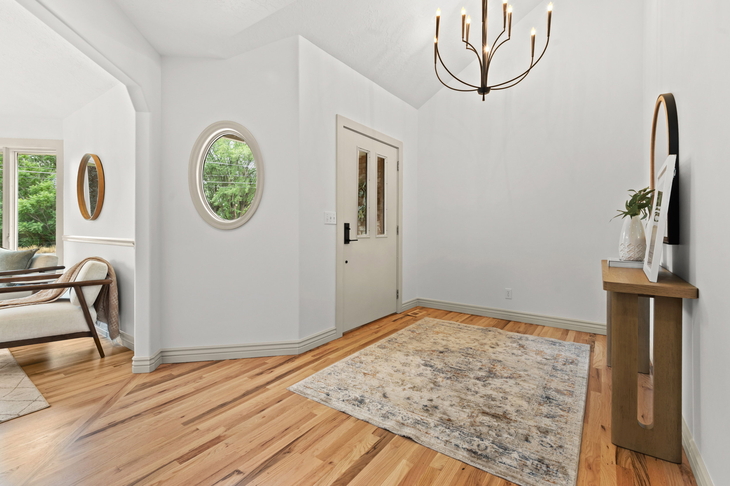 Vaulted entryway featuring a six-light candelabra chandelier, wood-finish flooring, a white paneled front door with glass inserts, and an oval window