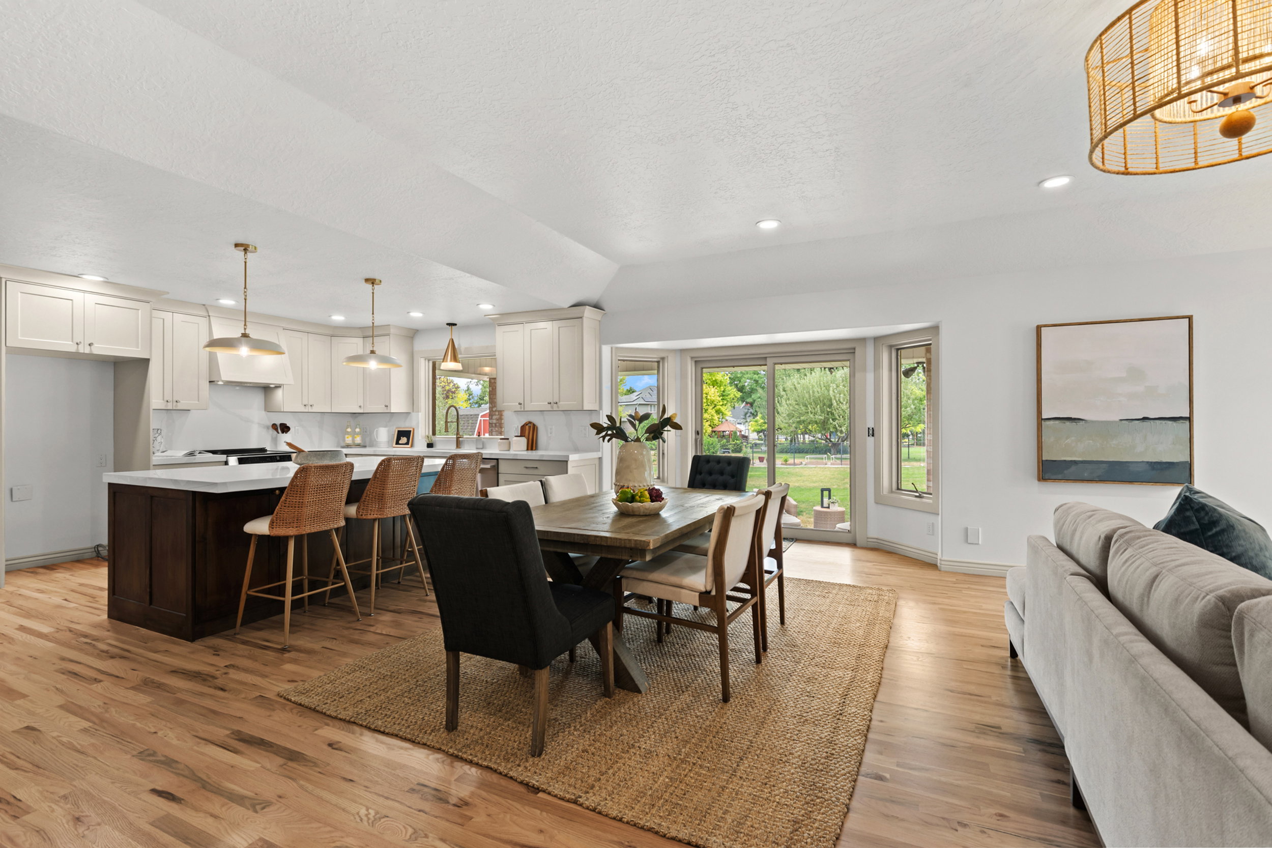 Open-concept living space featuring wood-finish flooring, a kitchen island with seating, white shaker cabinetry, a dining area, and sliding glass doors opening to the exterior