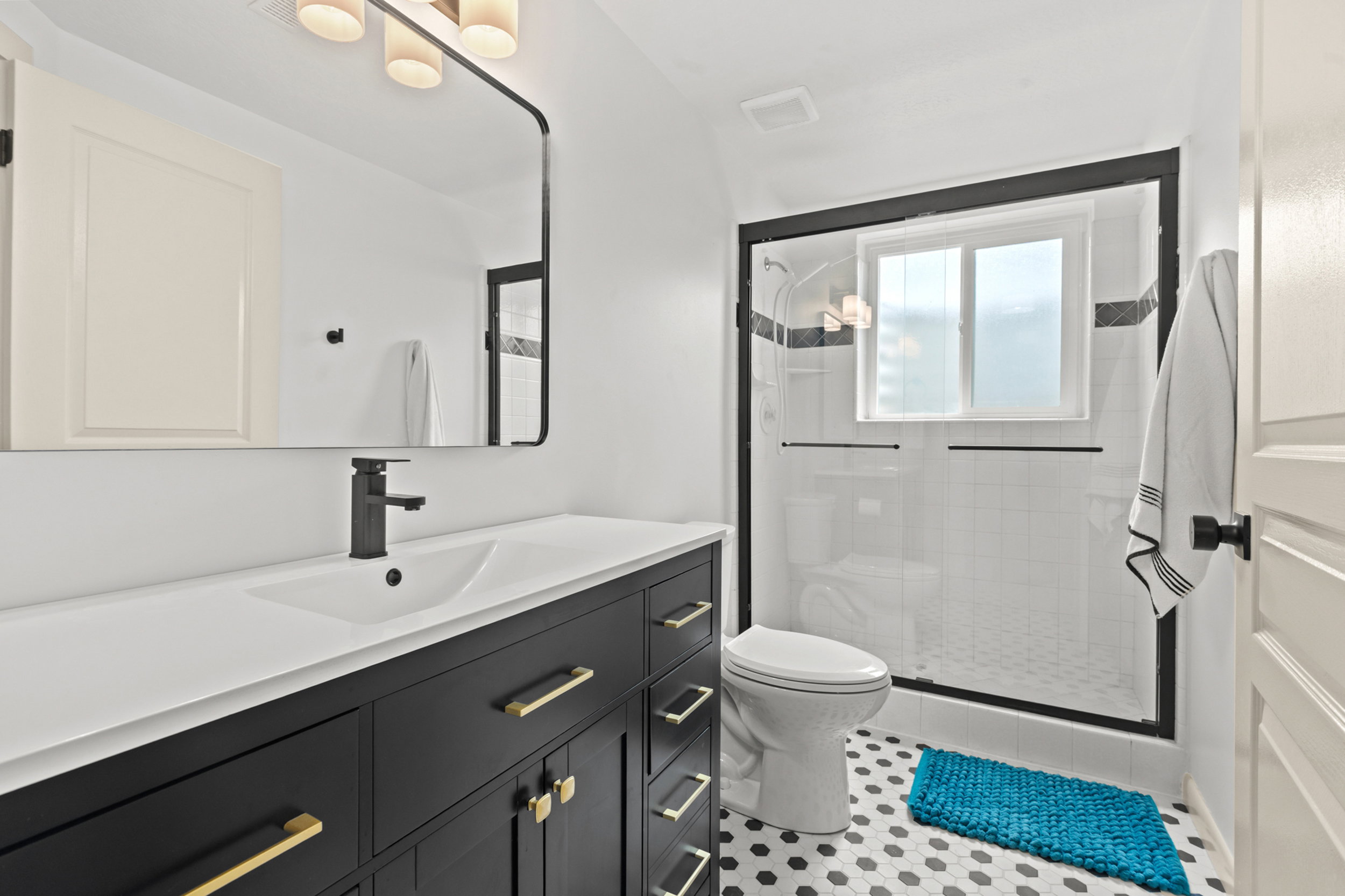 Bathroom featuring a dark wood-finish vanity with gold-tone hardware, a white integrated sink, a matte black faucet, and a large black-framed mirror