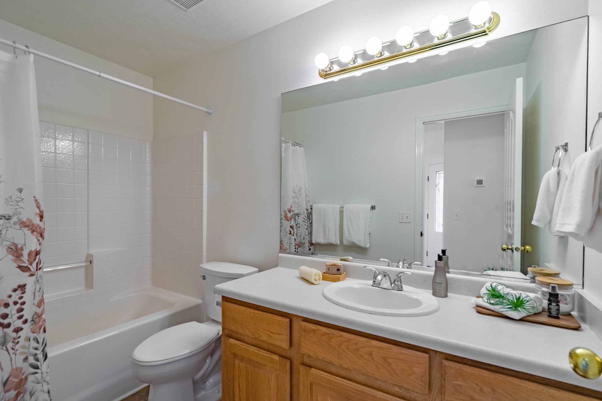 Full bathroom featuring a single vanity with wood-finish cabinetry, a white countertop, and a large mirror