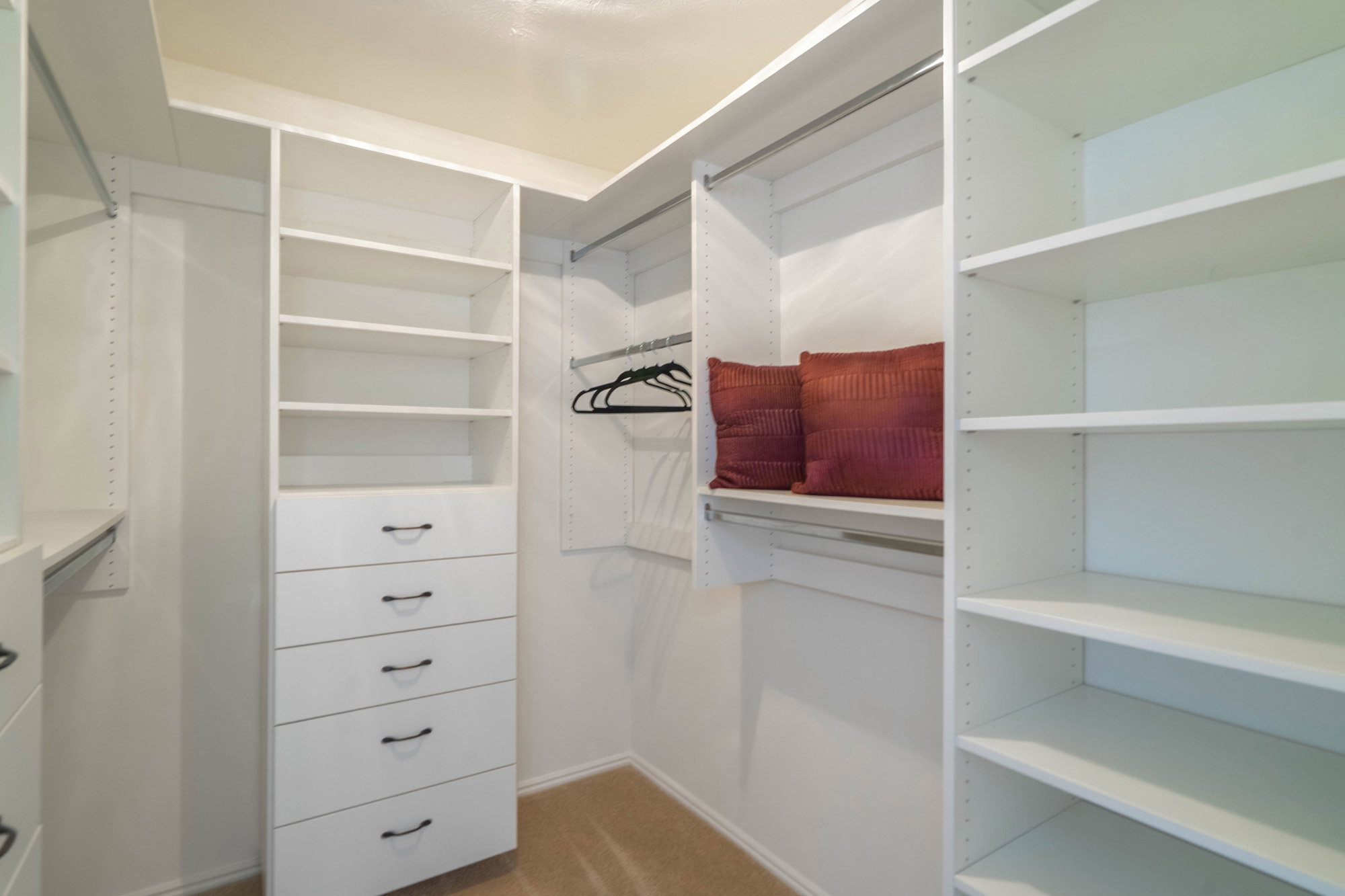 Walk-in closet featuring white built-in shelving, multiple hanging rods, and a five-drawer dresser unit with dark hardware