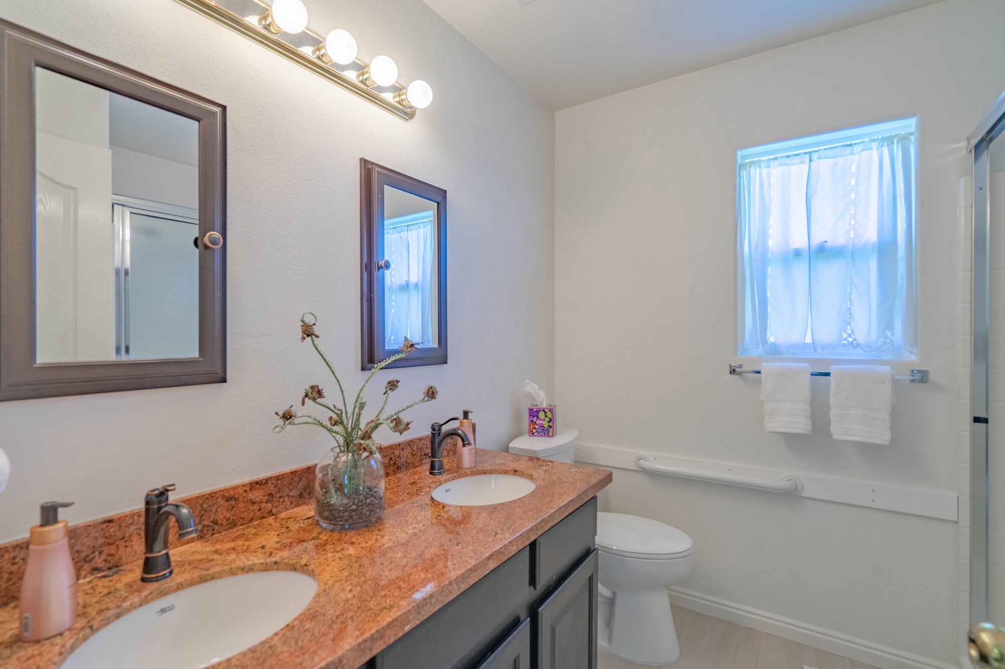 Dual vanity with a stone countertop, individual framed mirrors, and dedicated lighting