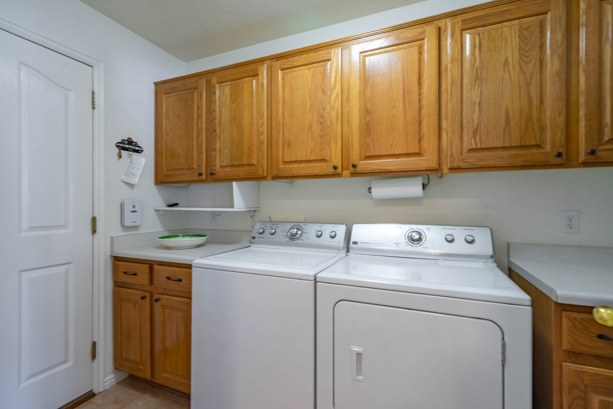 Laundry area featuring wood-finish cabinetry, white countertops, built-in shelving, and a paper towel dispenser