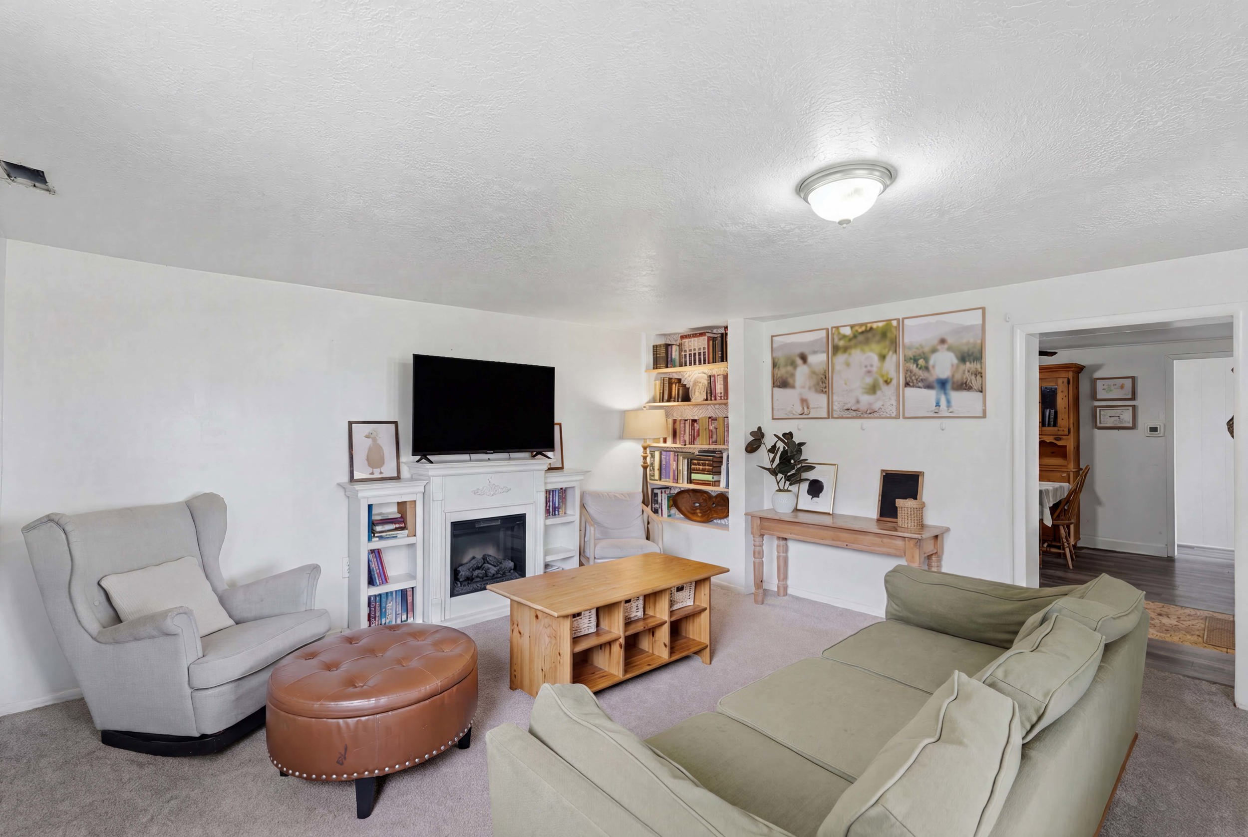 Living area featuring  built-in shelving, light-colored carpeting, a ceiling-mounted light fixture, and an arched doorway leading to an adjacent room with wood-finish flooring