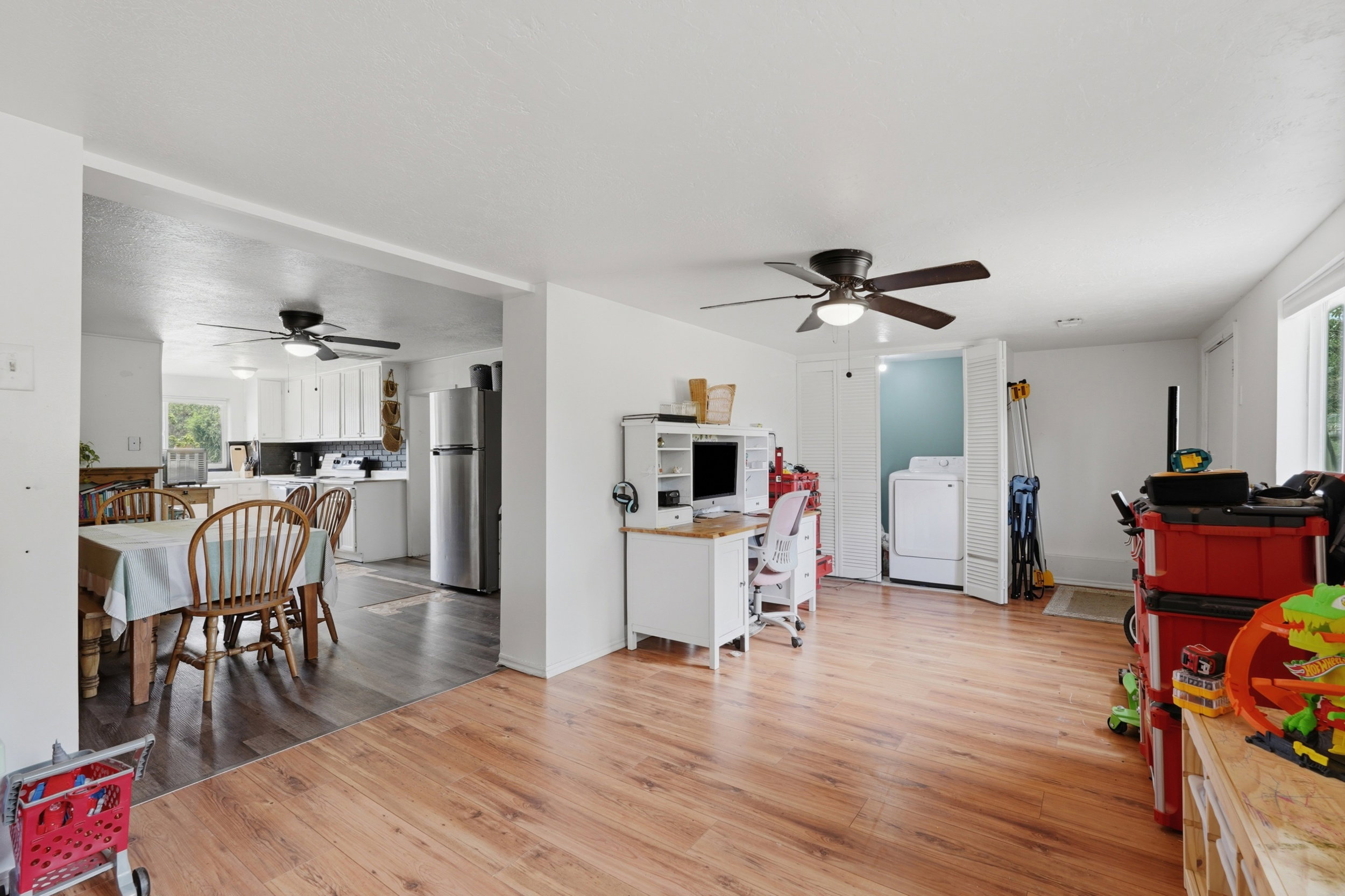Spacious living area featuring wood-finish flooring, a ceiling fan, and white walls