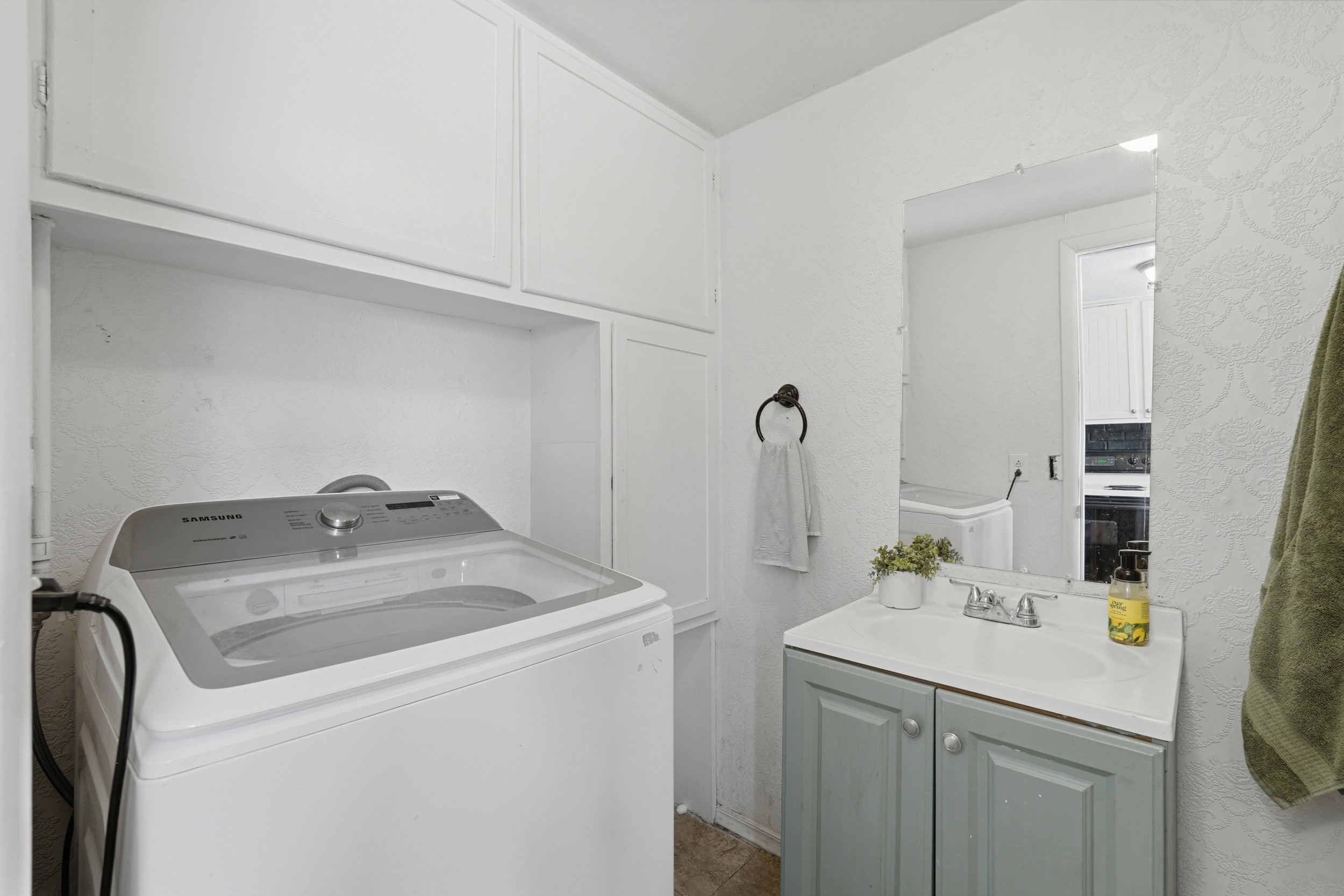 Dedicated utility space featuring overhead white cabinetry, a built-in shelf, a single-sink vanity with a light green cabinet, and a wall-mounted mirror