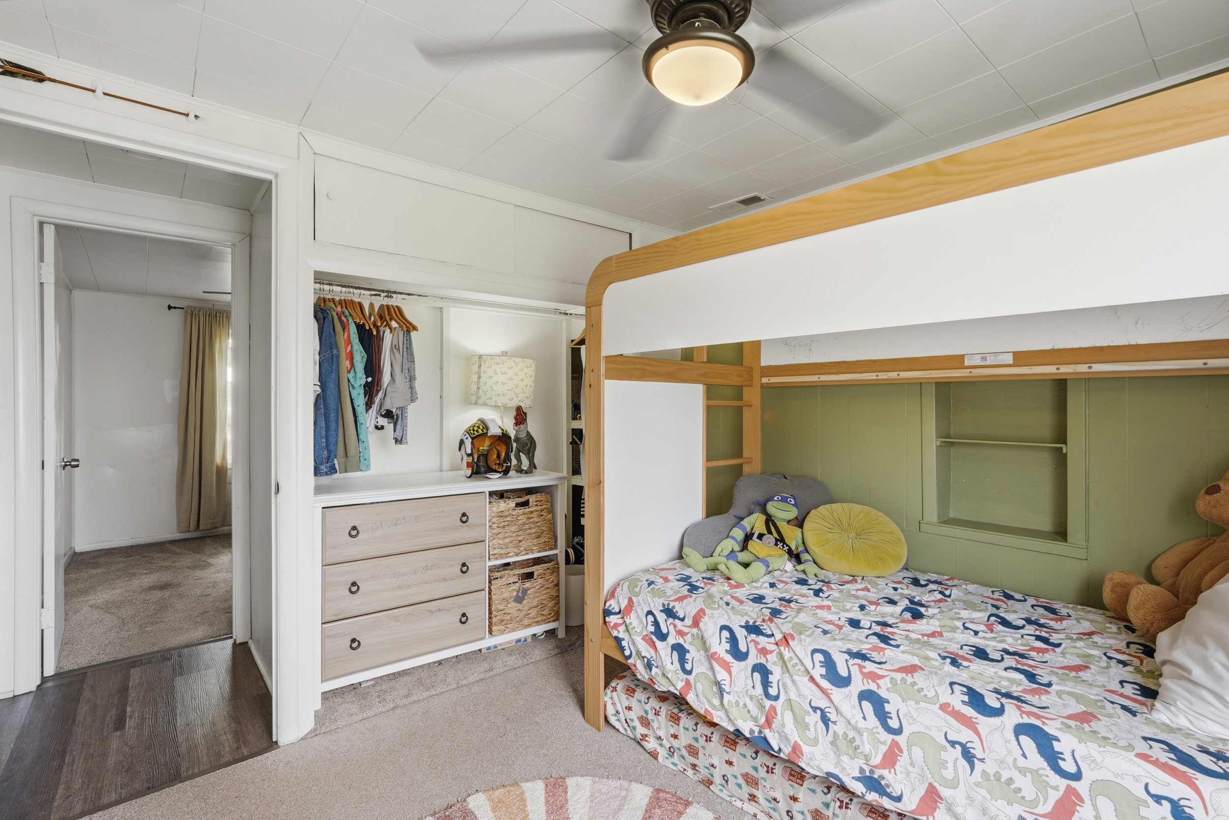 Bedroom featuring a built-in bunk bed, an integrated closet system with drawers and shelving, wood-finish flooring at the doorway, carpeted flooring, and an overhead ceiling fan