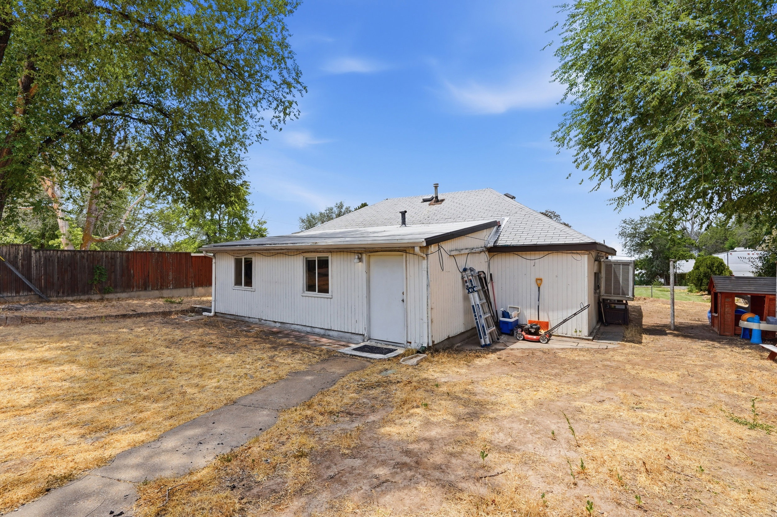 Spacious backyard featuring a large grass area, mature perimeter trees, and a wooden privacy fence