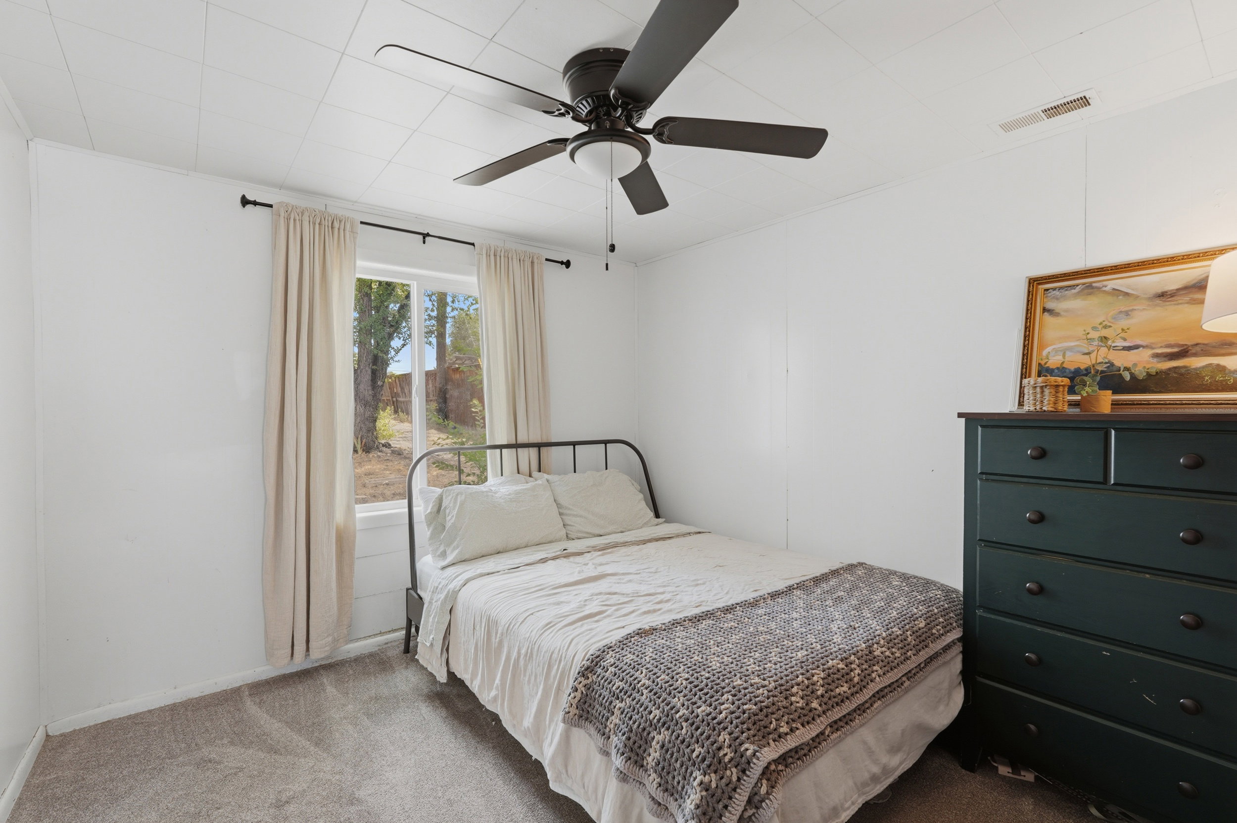 Recessed window with drapes, ceiling fan, carpet flooring, and white wall paneling