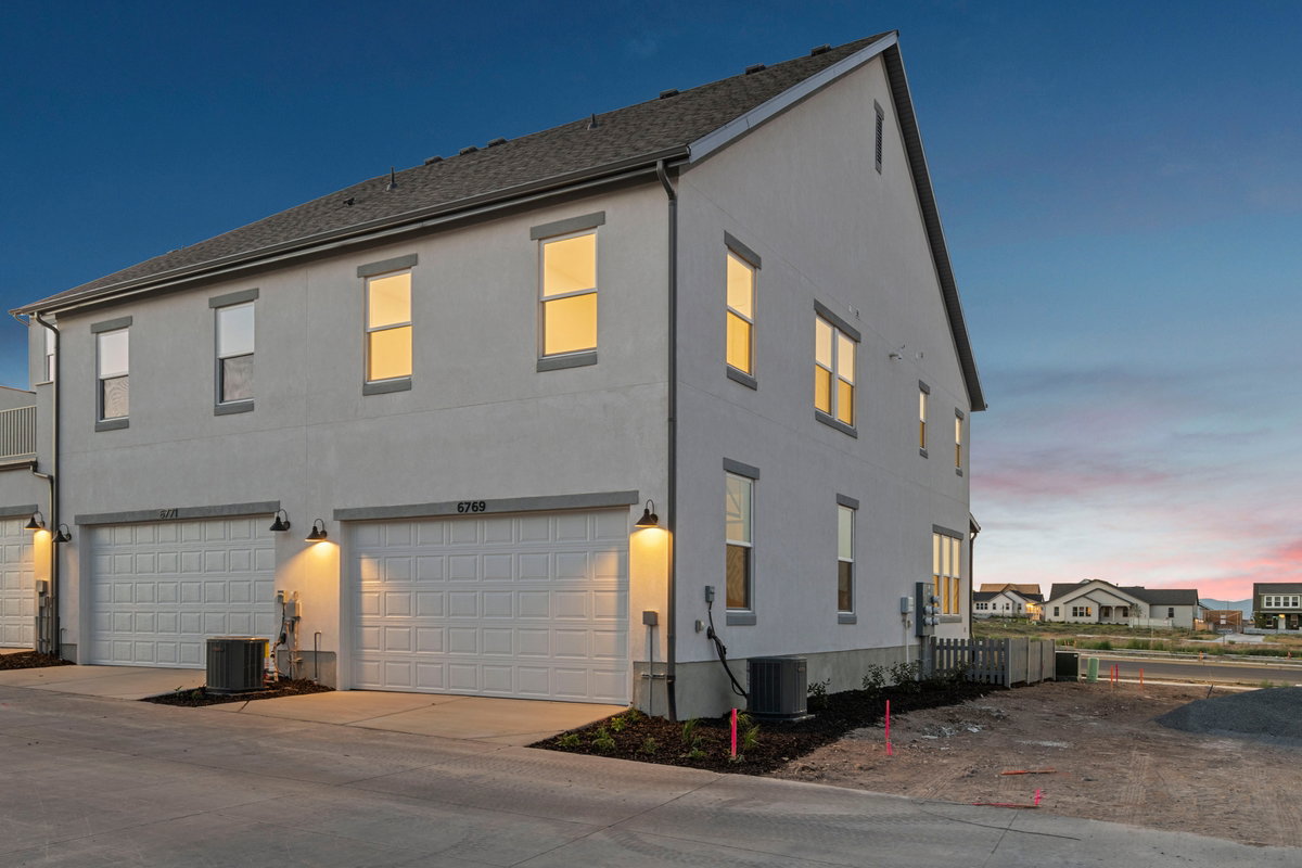 Contemporary multi-level residence featuring a light-toned stucco exterior, dark shingle roofing, and multiple windows with dark trim