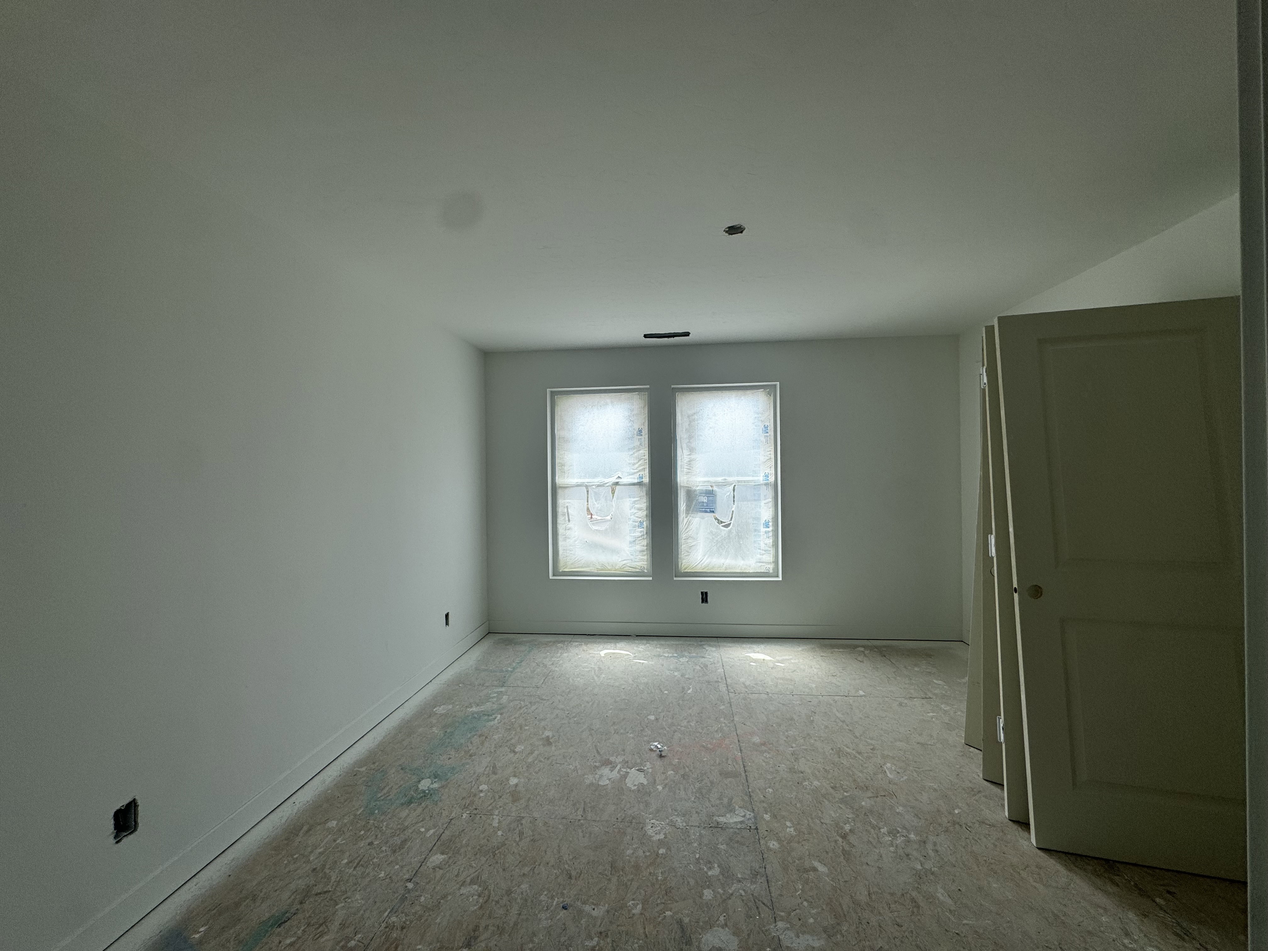 Unfinished interior space featuring light-toned walls, exposed subflooring, and two windows