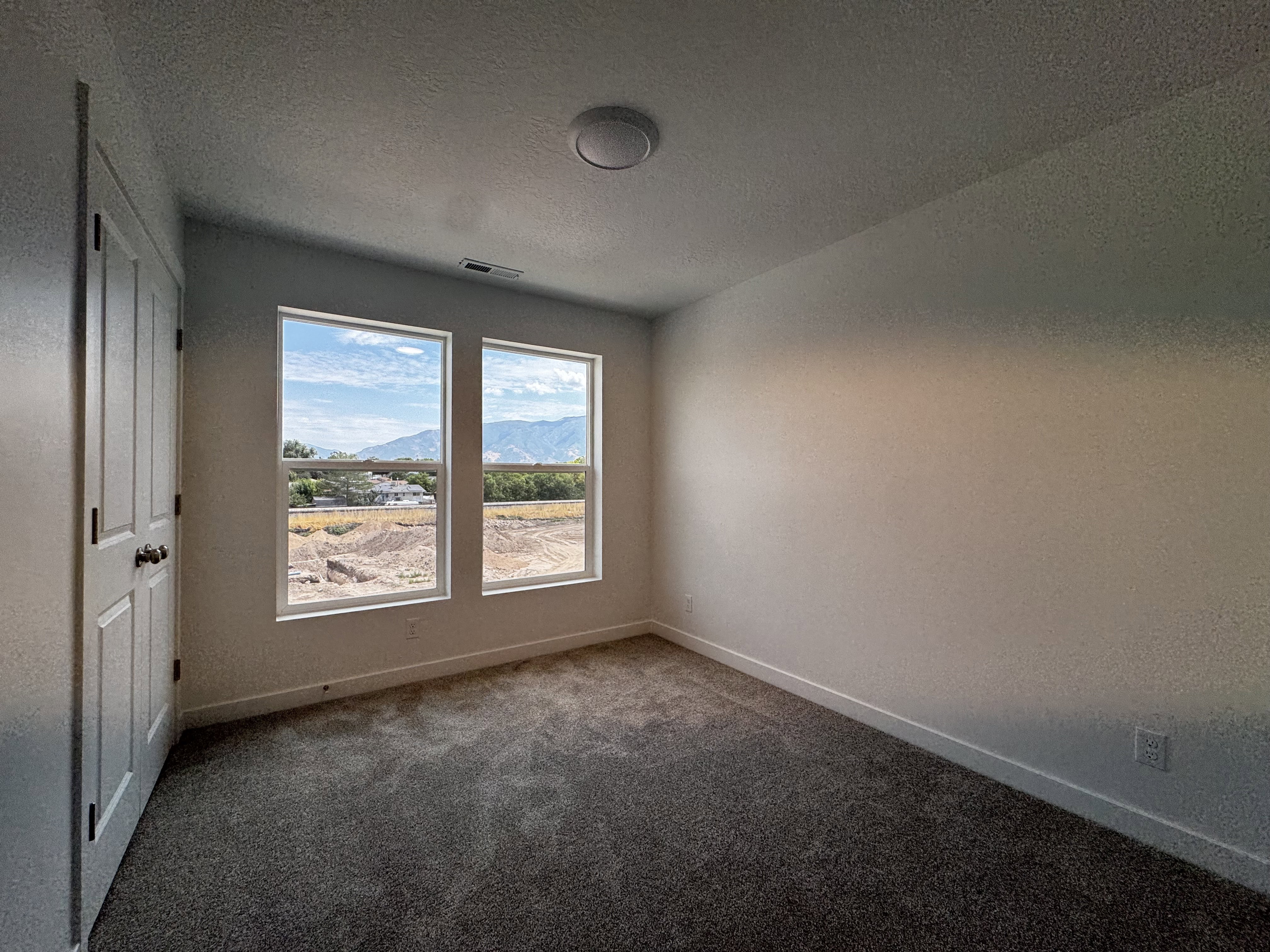 Room featuring two large windows with mountain scenery, neutral-toned carpeting, white baseboards, and a flush-mount ceiling light