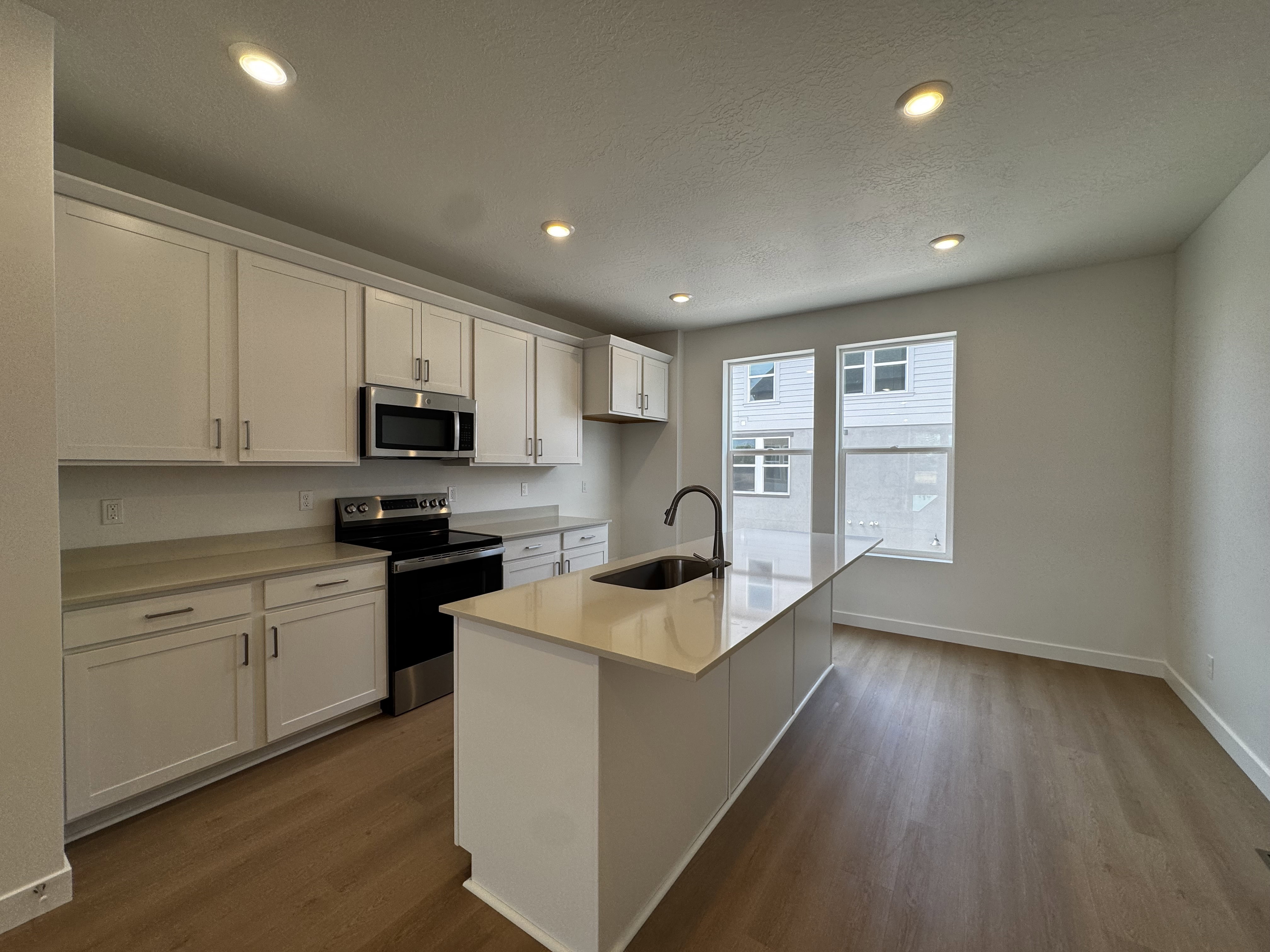 Contemporary kitchen featuring white cabinetry, a large center island with integrated sink, stainless steel appliances, and wood-finish flooring