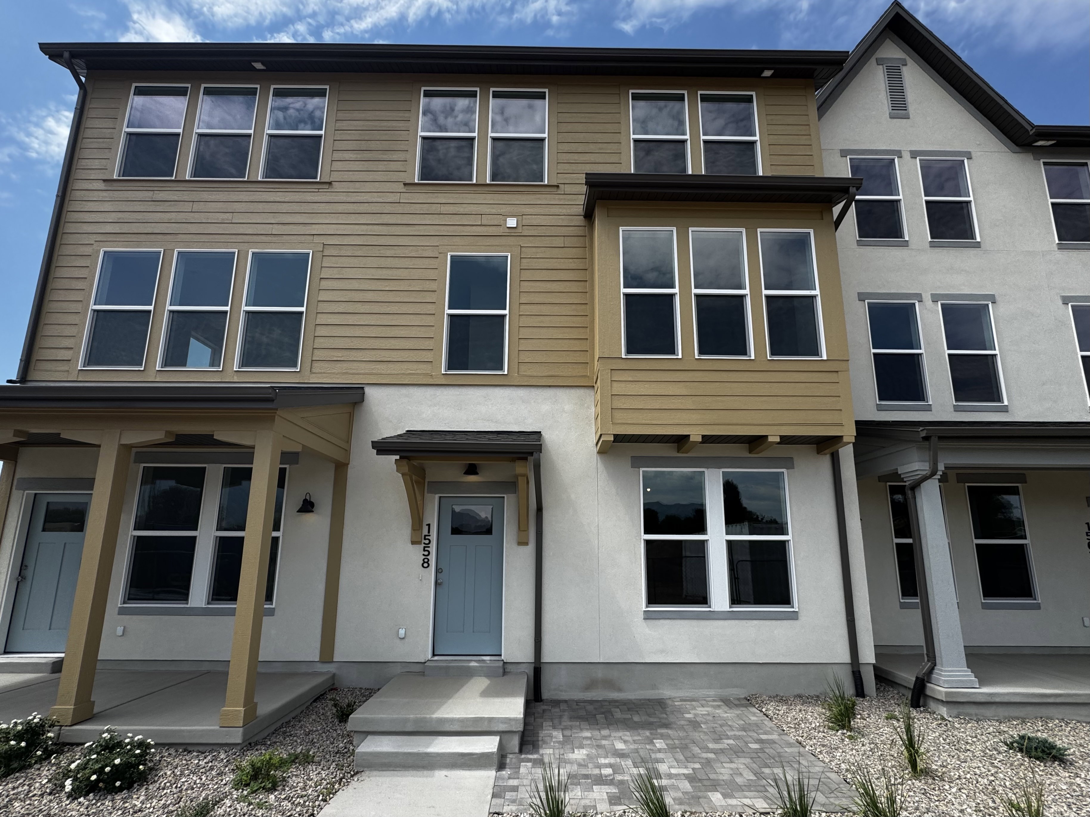 Multi-level townhome featuring a light blue entry door, decorative corbels, and a prominent bay window with horizontal siding