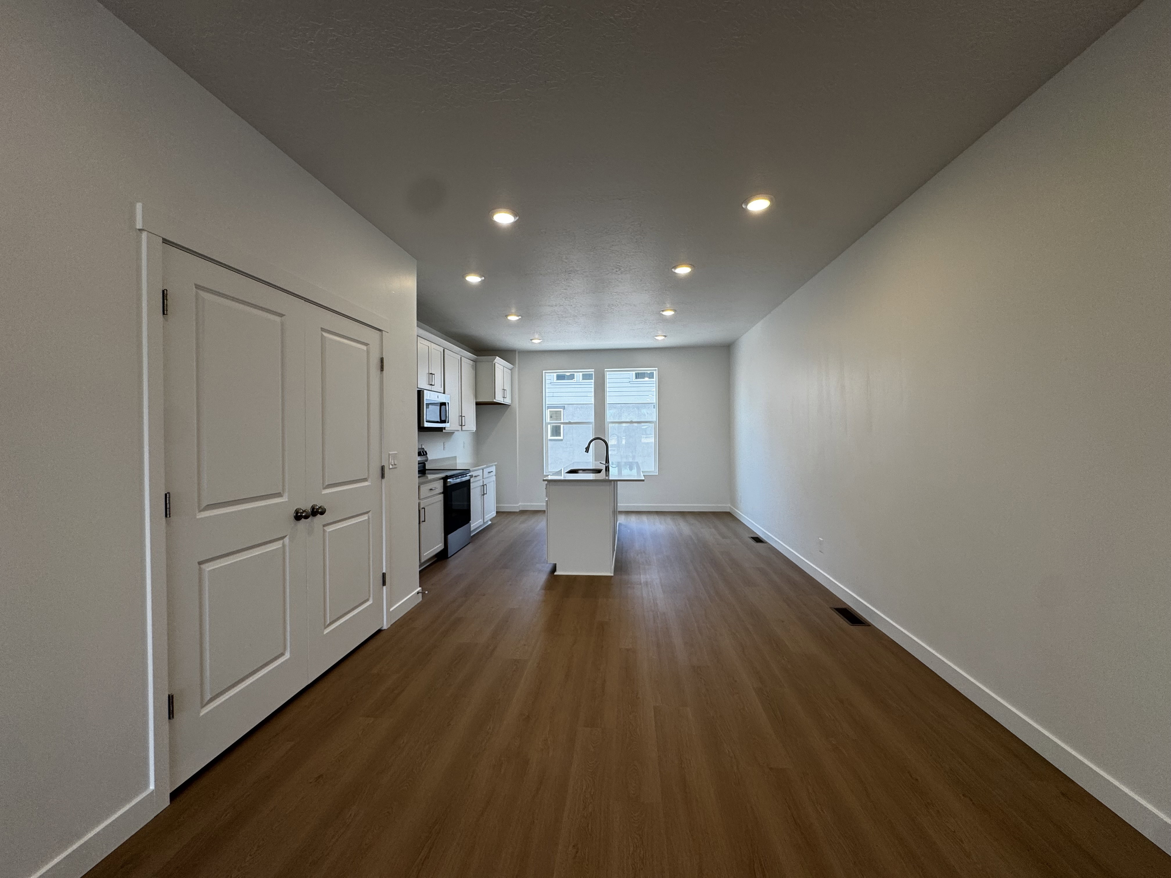 Open-concept living area featuring wood-finish flooring, recessed lighting, and a kitchen with white cabinetry, a central island, and stainless steel appliances