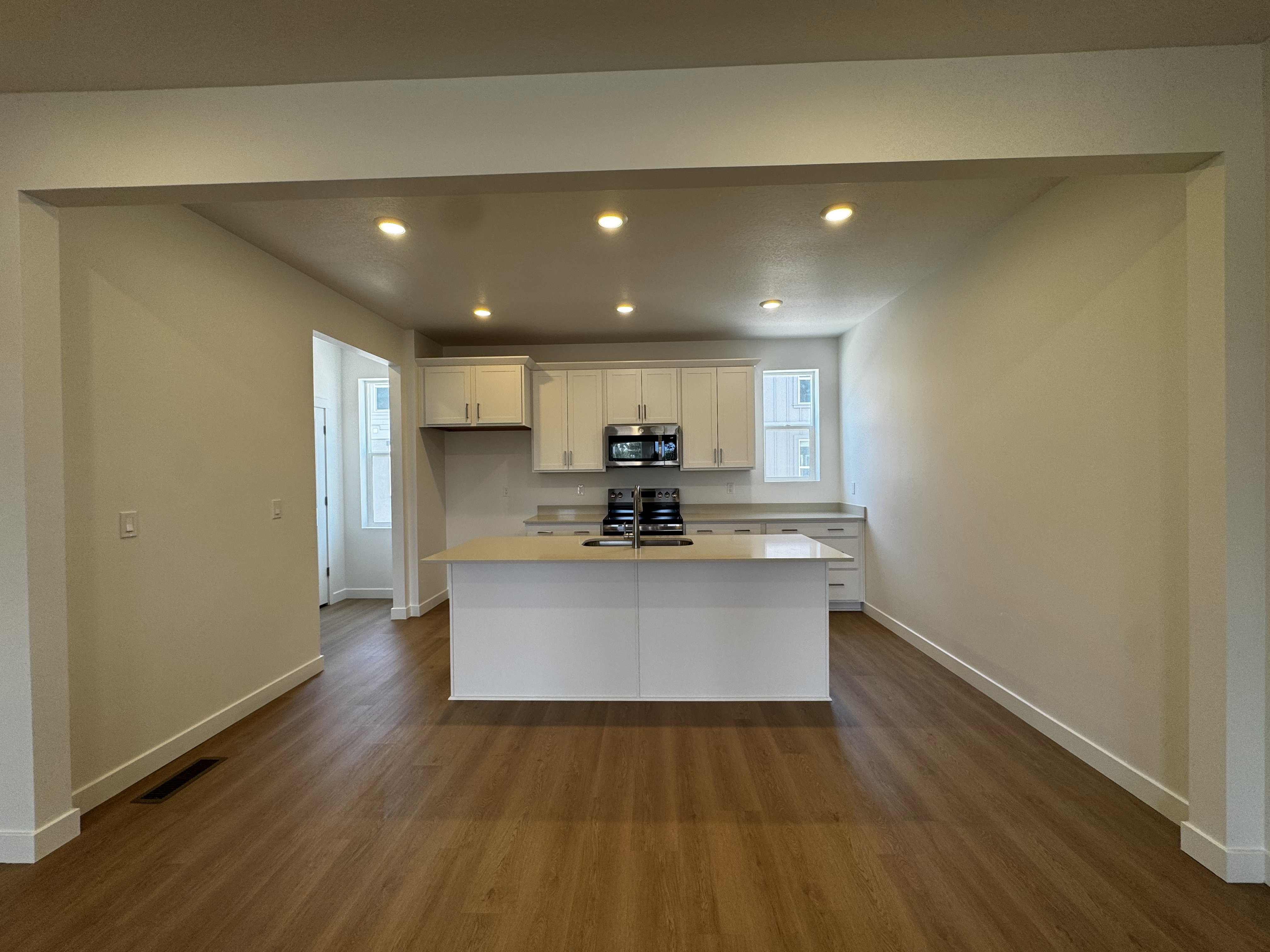 Open-concept kitchen and living area featuring wood-finish flooring, recessed lighting, a kitchen island with sink, white shaker cabinetry, and stainless steel appliances