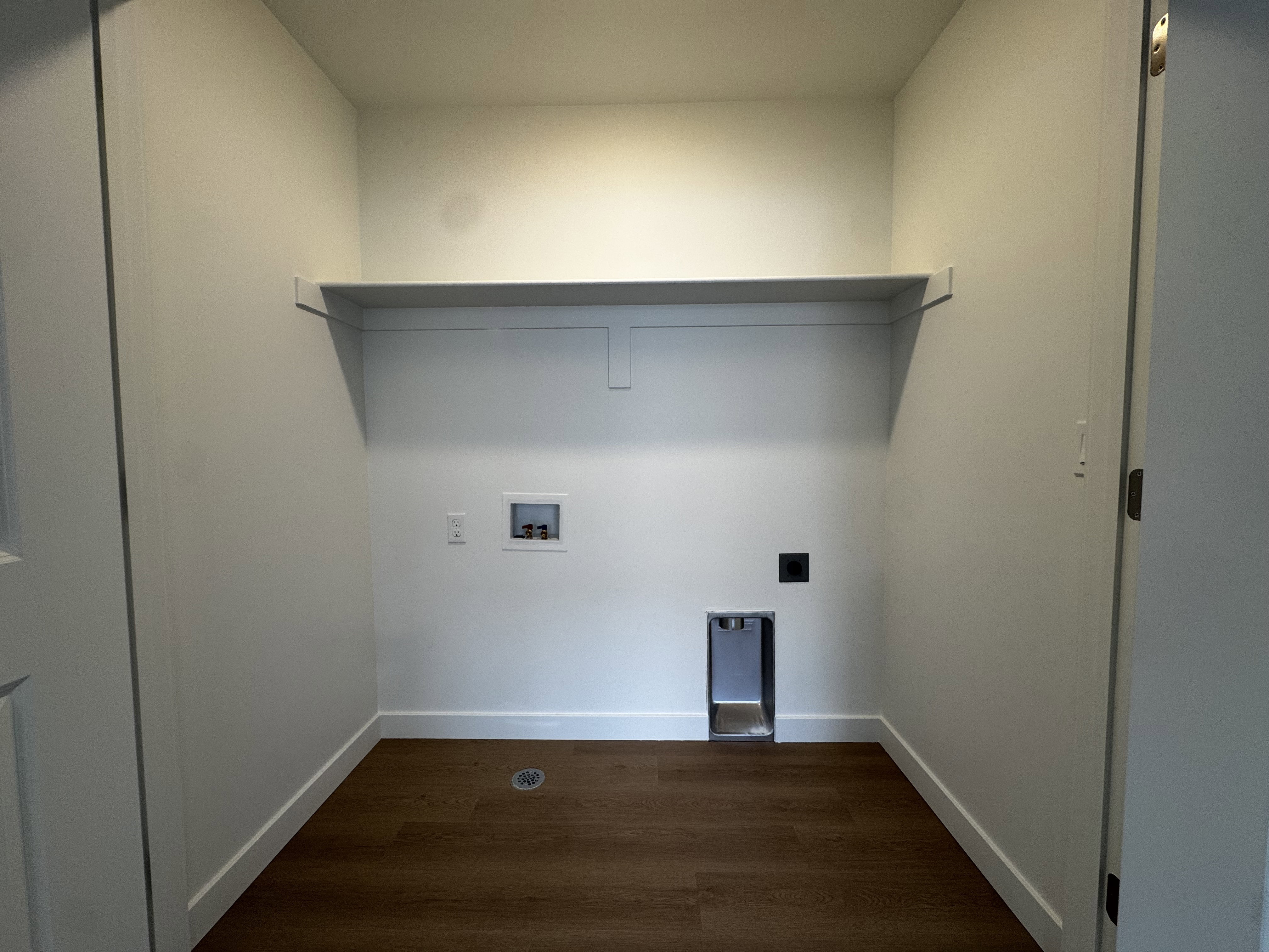 Dedicated laundry area featuring a wall-mounted shelf, bright white walls, and wood-finish flooring