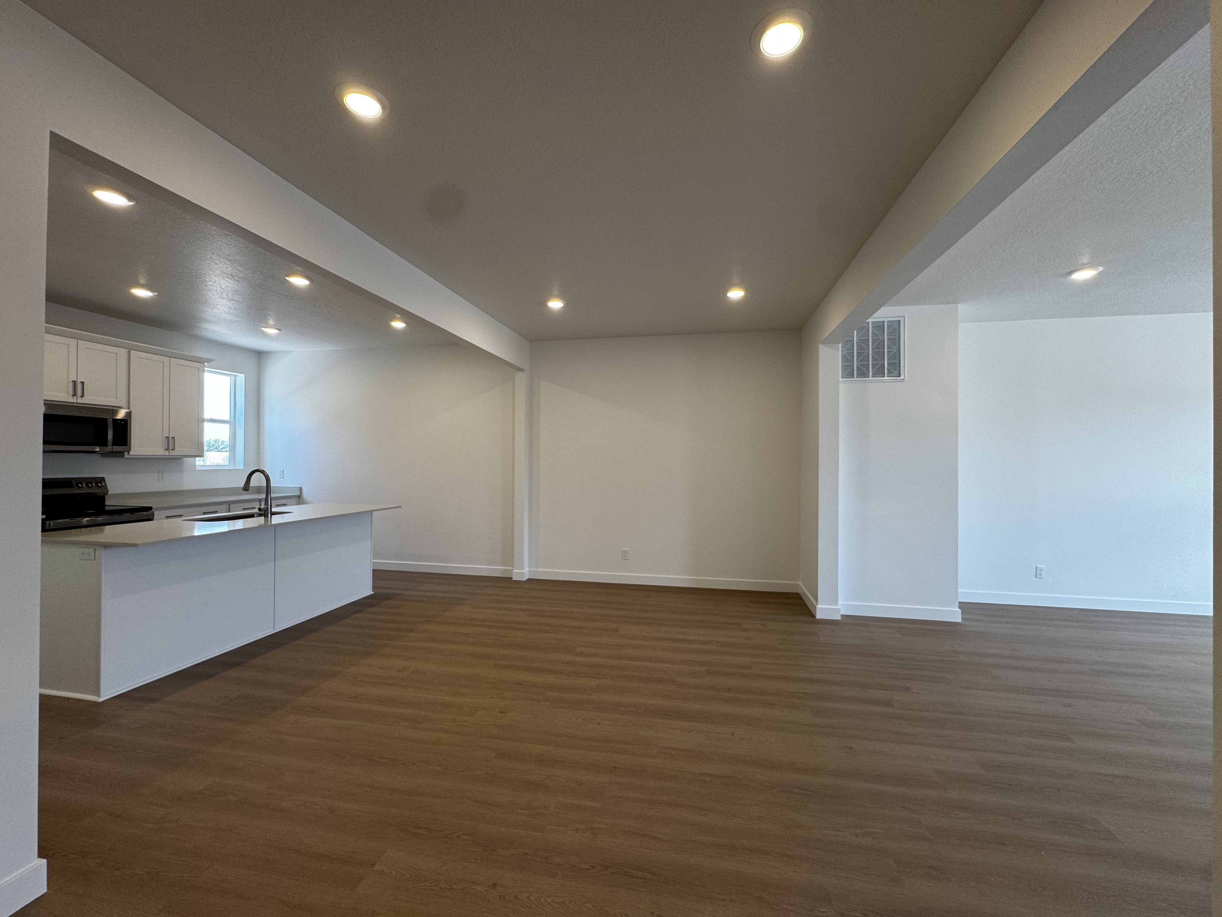 Open-concept living space featuring wood-finish flooring, recessed lighting, and a kitchen island with an undermount sink